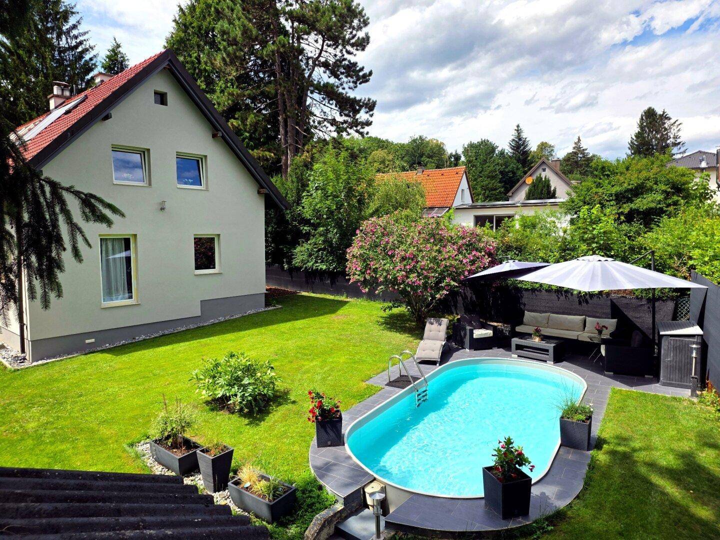 Weitläufiger Garten mit Pool, Liegewiese und dem Wohnhaus im Hintergrund unter blauem Himmel.