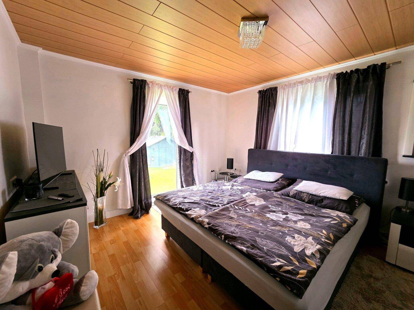 Gemütliches Schlafzimmer mit Doppelbett, Holzdecke und Zugang zum Außenbereich.