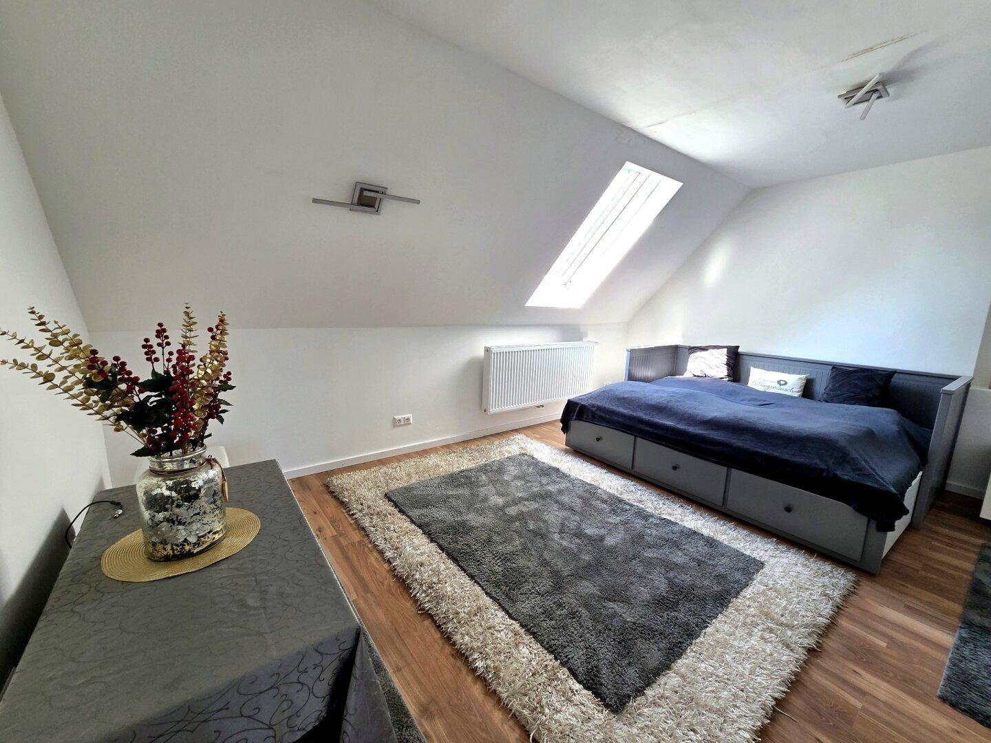 Helles Schlafzimmer im Dachgeschoss mit Dachfenster, Holzboden und Stauraumbett.