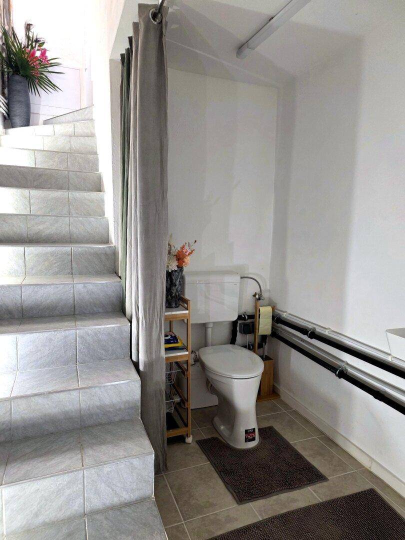 Praktisches WC unter der Treppe mit Vorhang und kleinem Waschbecken.
