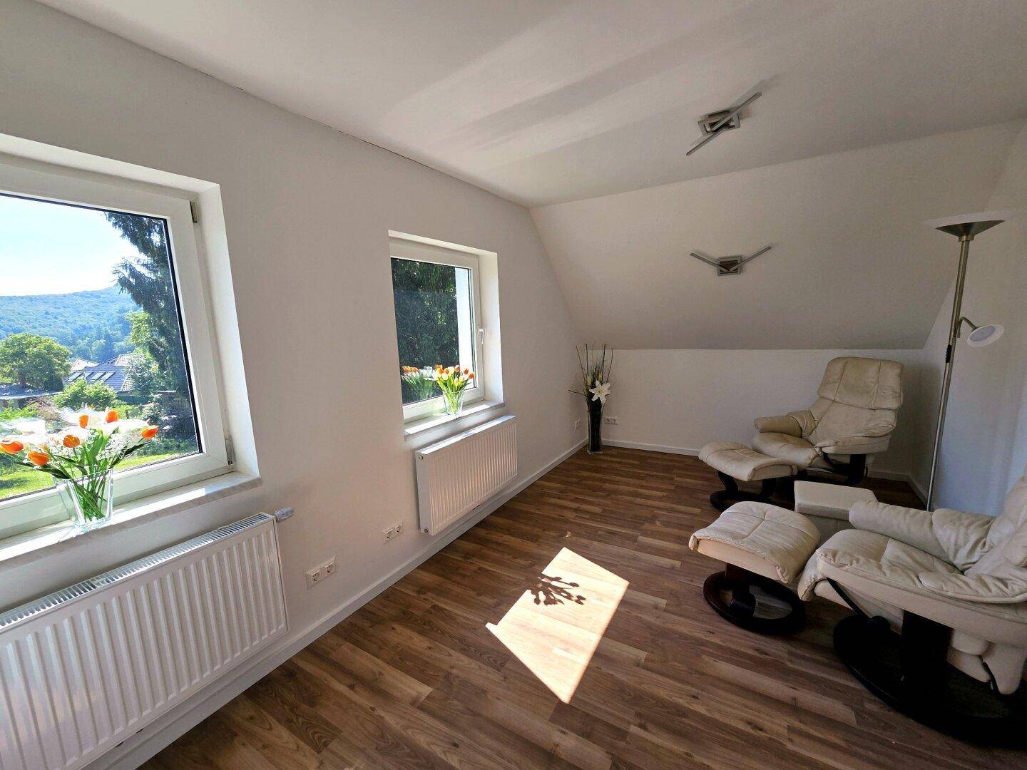 Heller Raum mit zwei Fenstern, Holzboden und bequemen Sesseln, ideal als Büro oder Gästezimmer.