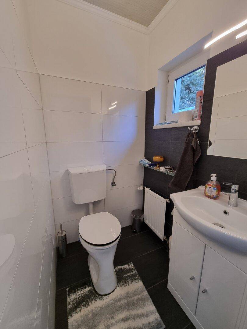 Separates WC mit Fenster, wandmontierter Toilette und kleinem Waschbecken.