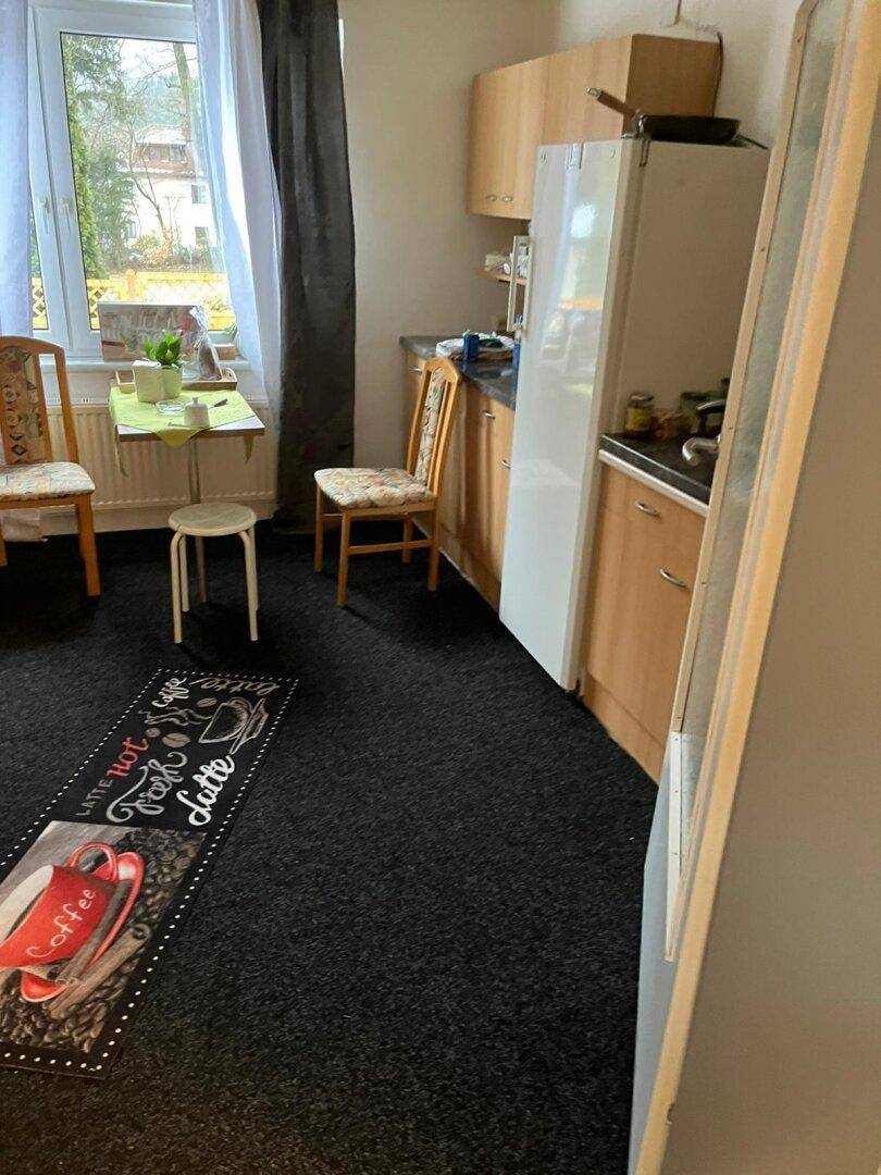 Funktionale Küche mit einfachen Holzschränken, Kühlschrank und Fenster.