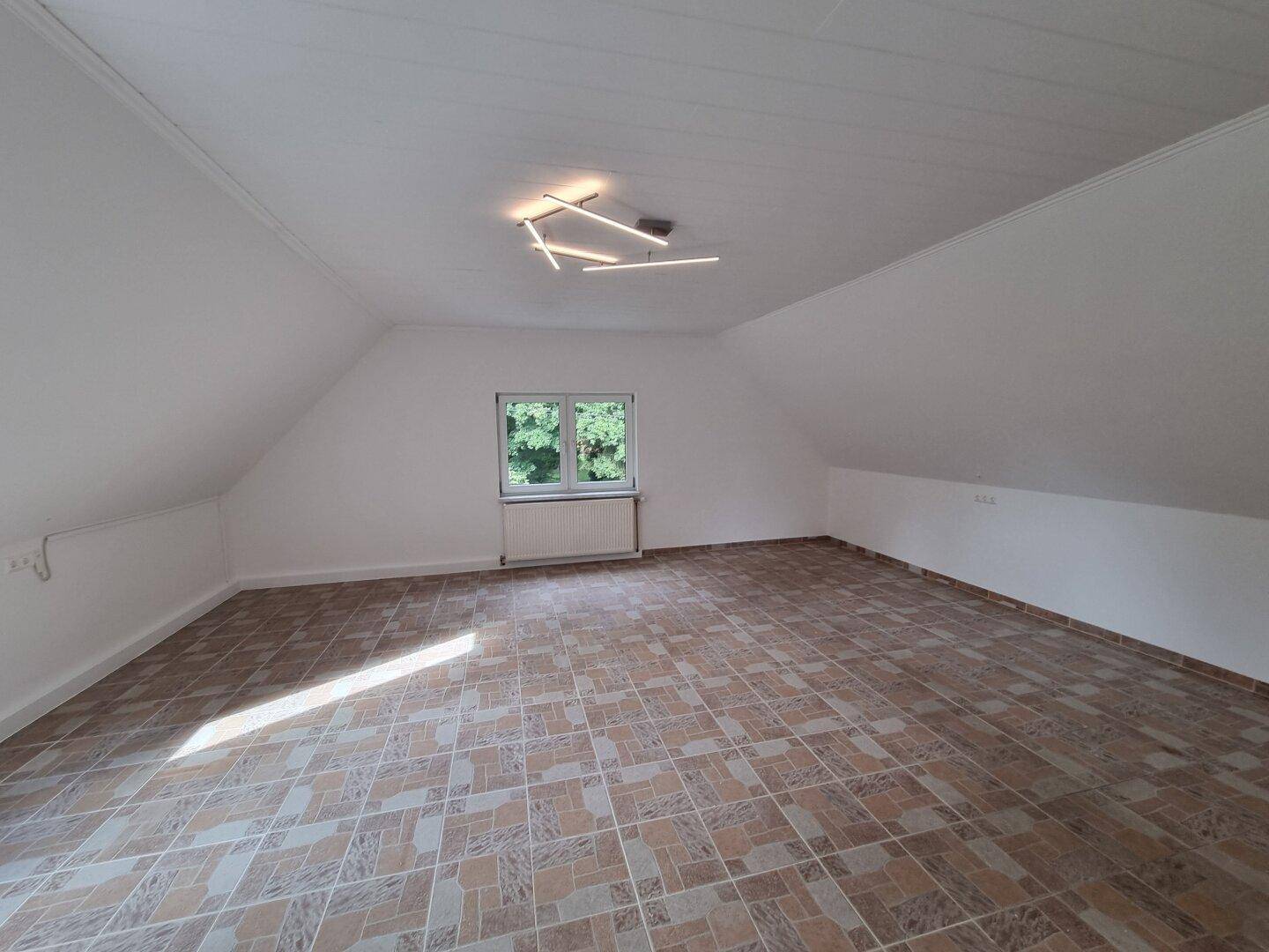 Geräumiger Dachbodenraum mit Fenster und Fliesenboden, ideal für Ausbau oder Lagerung.