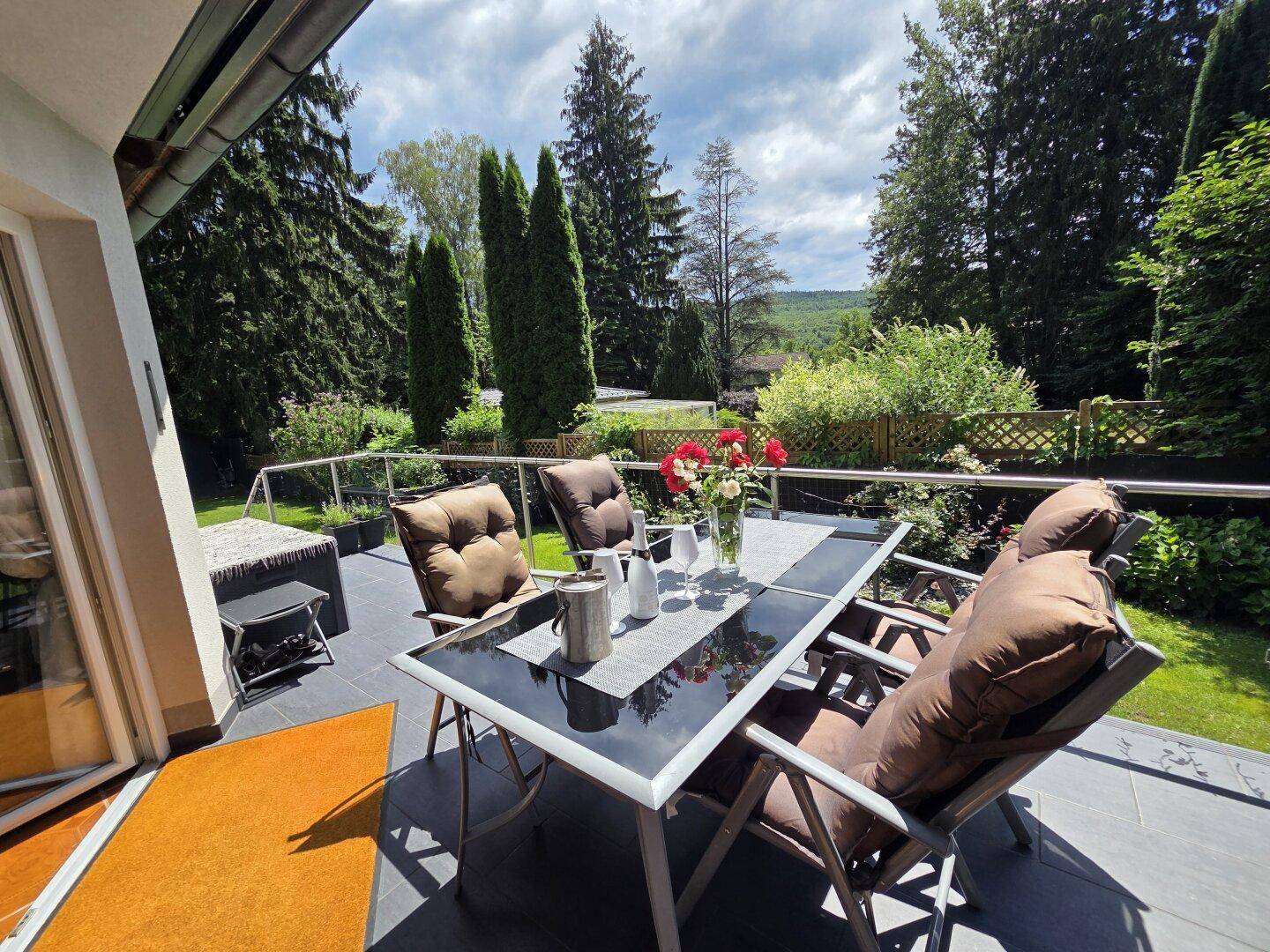 Heller Balkon mit Esstisch und Stühlen, umgeben von viel Grün und mit Blick in die Natur.