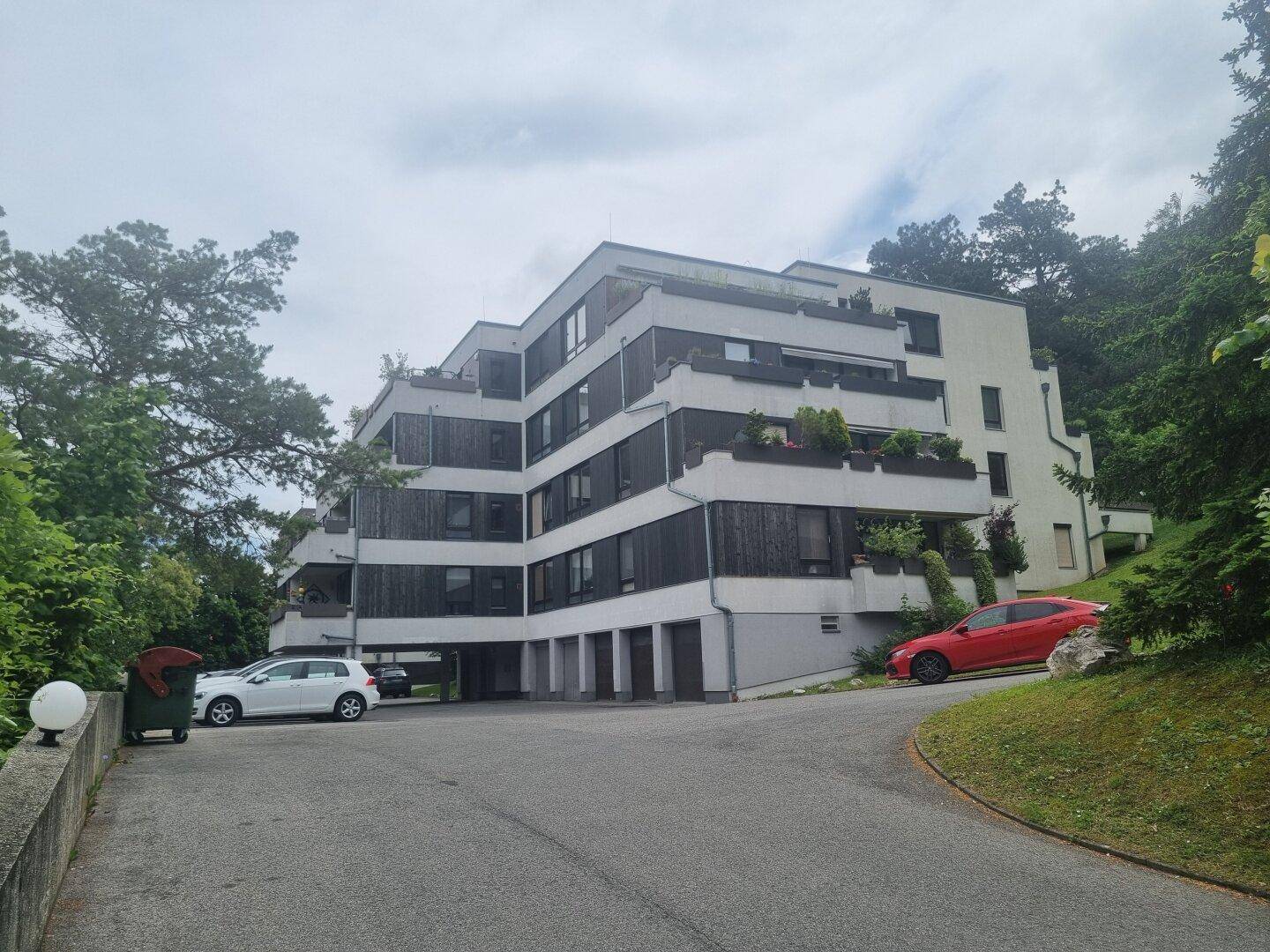 Modernes Mehrfamilienhaus mit mehreren Balkonen, umgeben von viel Grün.