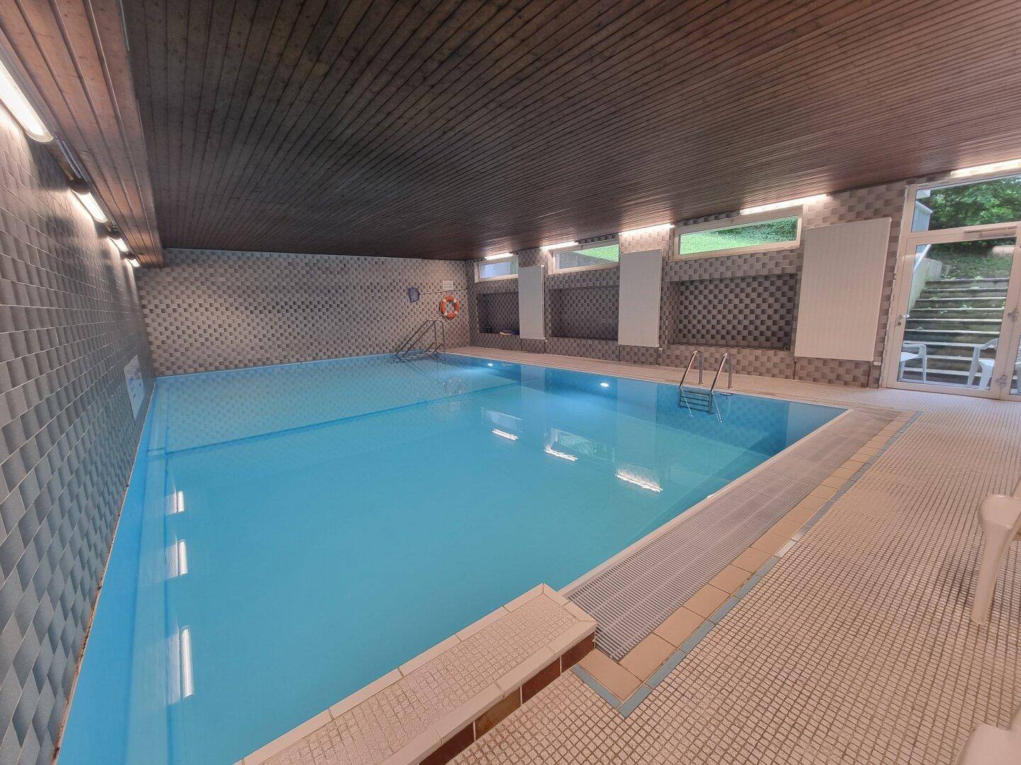 Geräumiger Innenpool mit blauen Fliesen und Zugang zum Außenbereich.