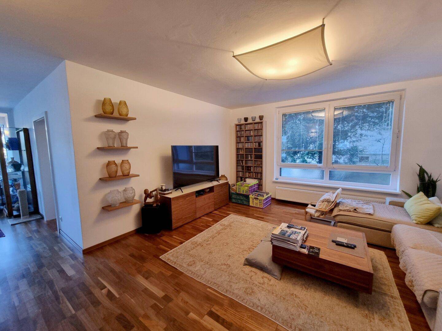 Gemütliches Wohnzimmer mit Holzboden, großem Fenster und TV-Möbeln.