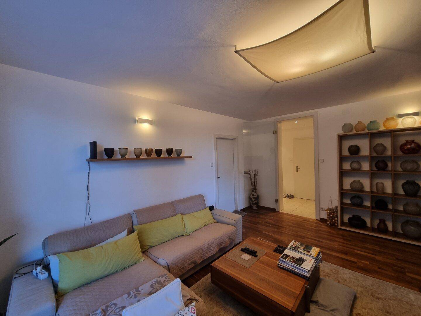 Wohnzimmer mit beigem Sofa, Holzboden und Zugang zu einem weiteren Raum.