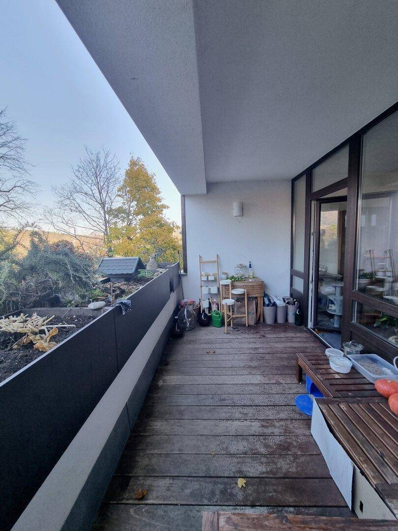 Geräumiger Balkon mit Holzboden, Sitzgelegenheiten und Blick ins Grüne.