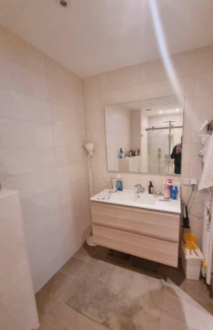Badezimmer mit modernem Waschtisch, großem Spiegel und hellen Fliesen.