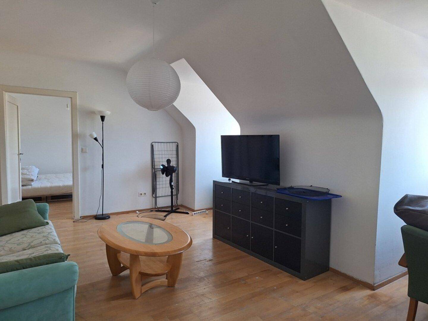 Wohnzimmer im Dachgeschoss mit schrägen Wänden, Holzfußboden und TV-Möbeln.