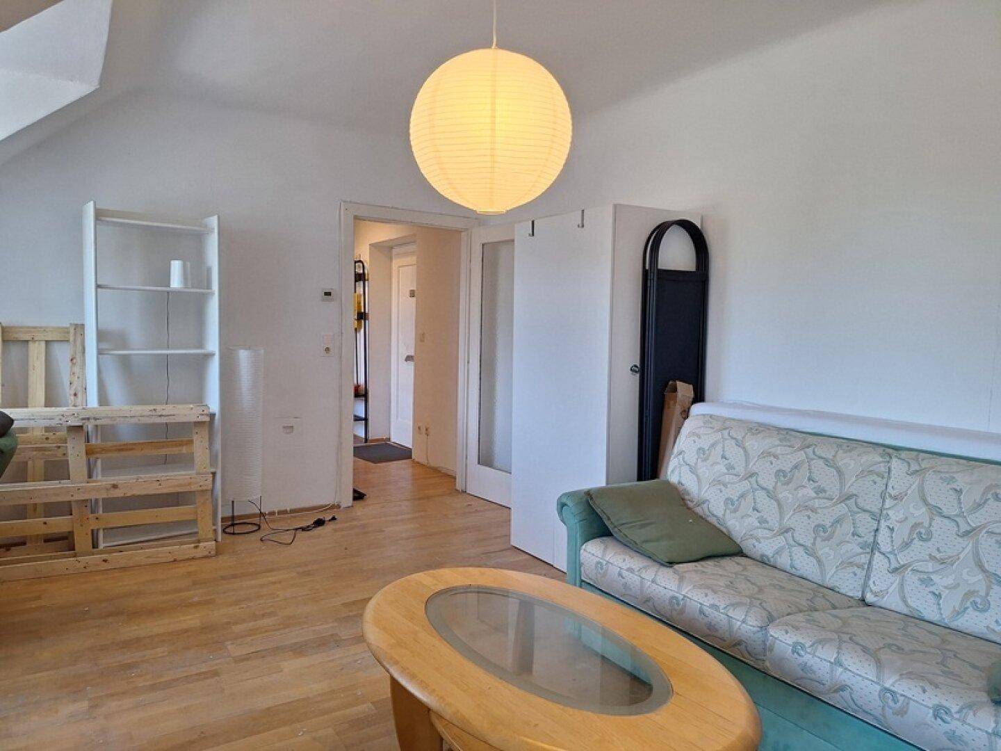 Wohnzimmer mit Holzfußboden, Sofa und einer Papierlampe, die zu einem Flur führt.