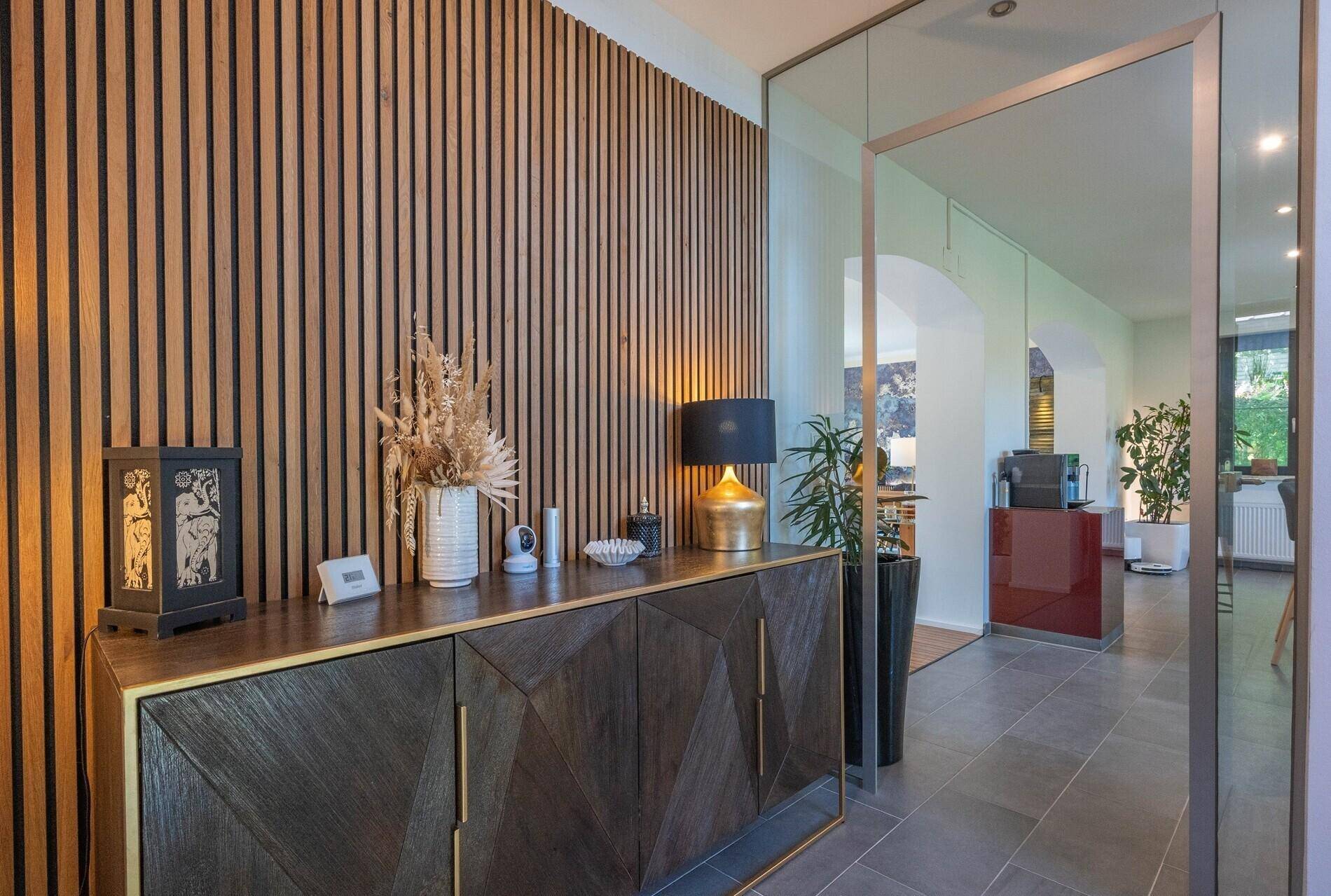 Moderner Flur mit Holzlamellenwand, Sideboard und dunklem Fliesenboden.