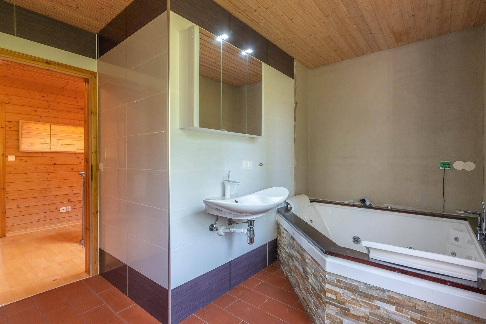 Badezimmer mit Whirlpool-Badewanne, Einzelwaschbecken und Holzdecke.