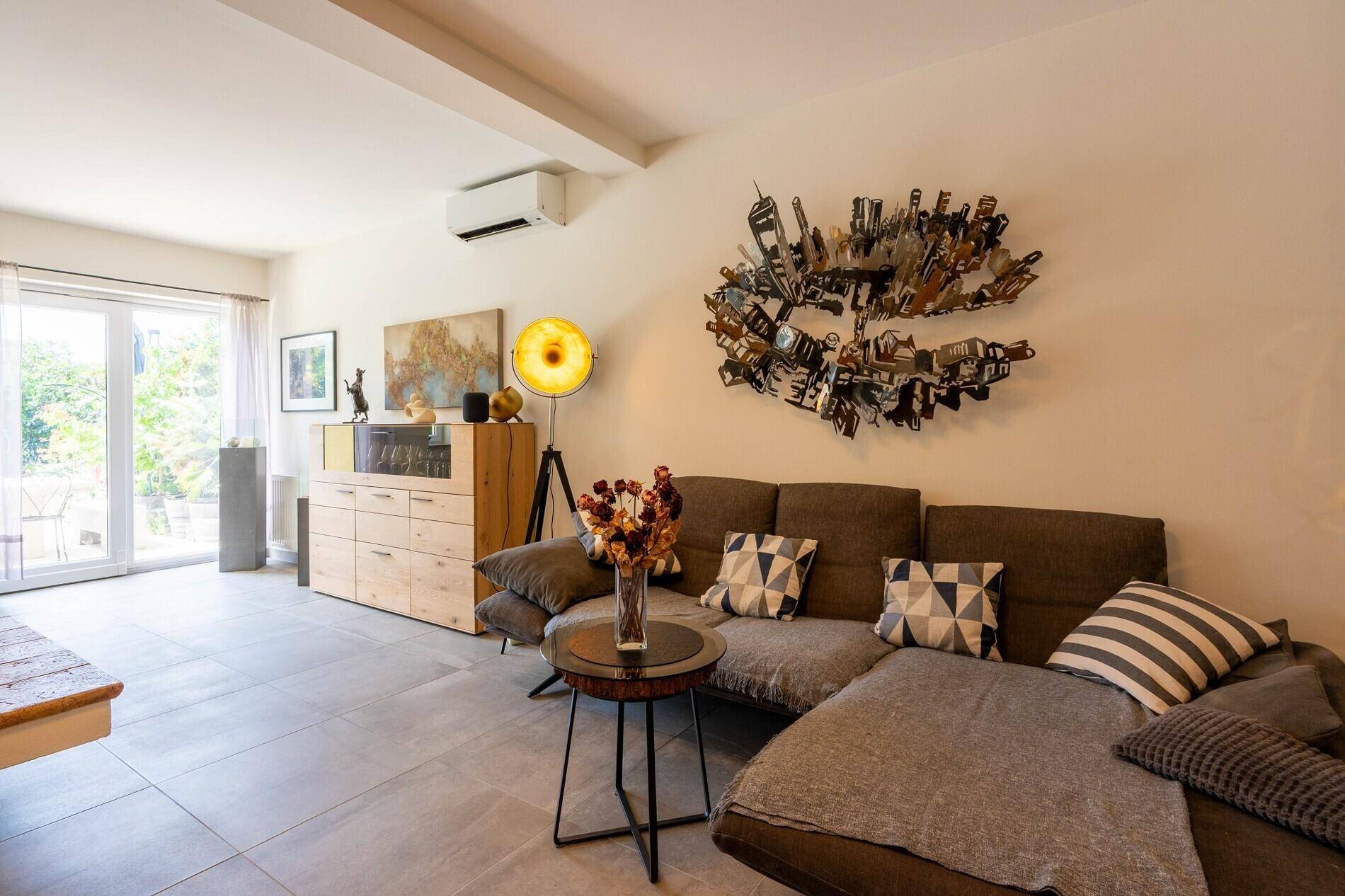 Gemütliches Wohnzimmer mit großem Sofa, modernen Kunstwerken und Zugang zum Garten.