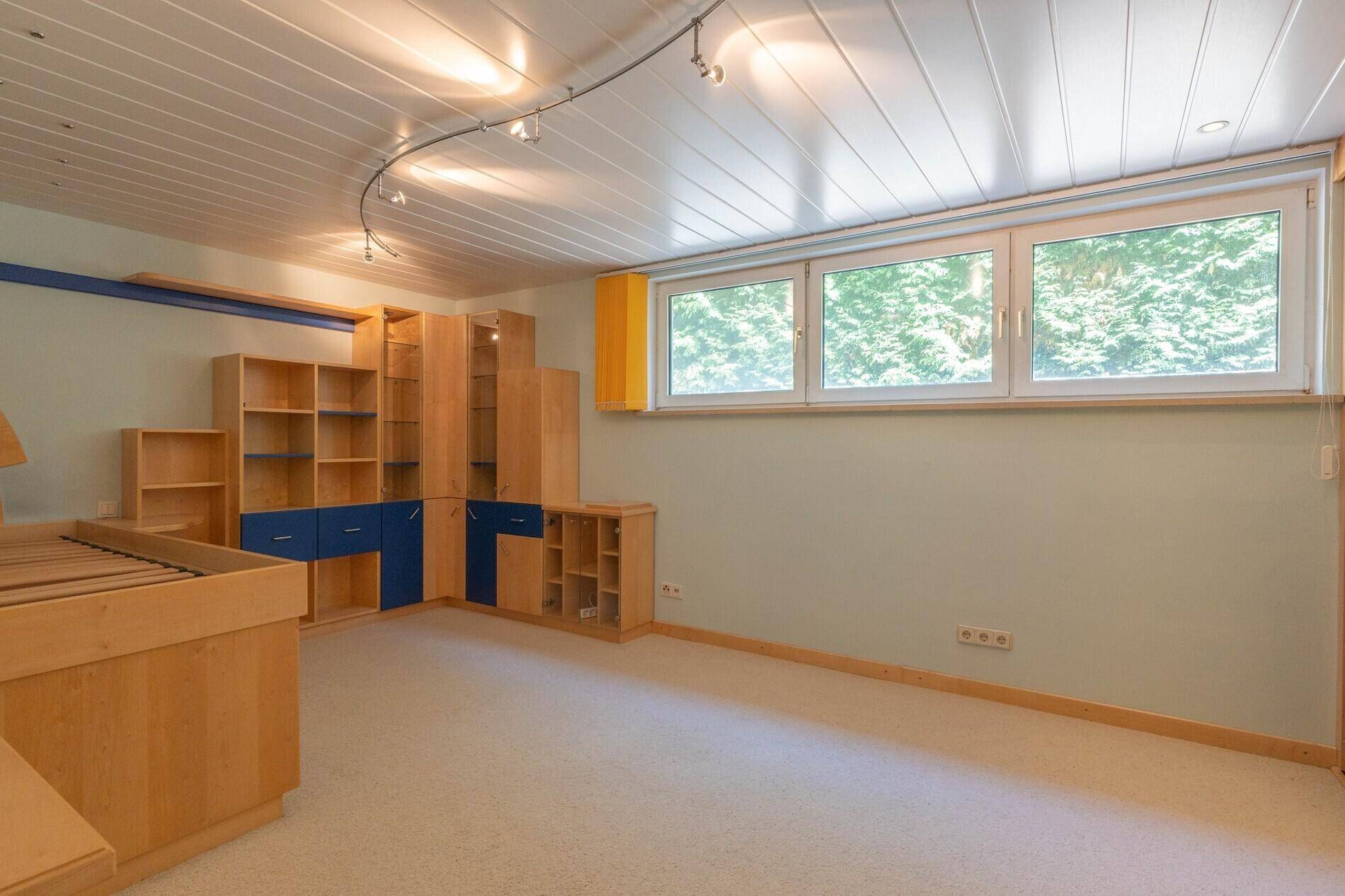 Kinderzimmer mit hellgrünen Wänden, Holzmöbeln mit blauen Akzenten und großen Fenstern.