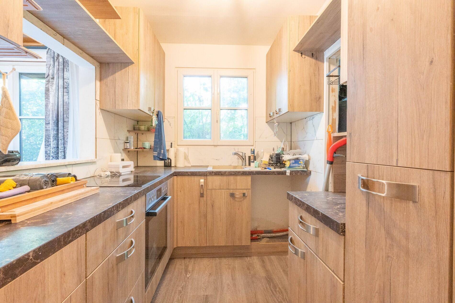 Funktionale Küche mit Holzoptik-Schränken, Einbauherd und Fenster mit Blick ins Grüne.