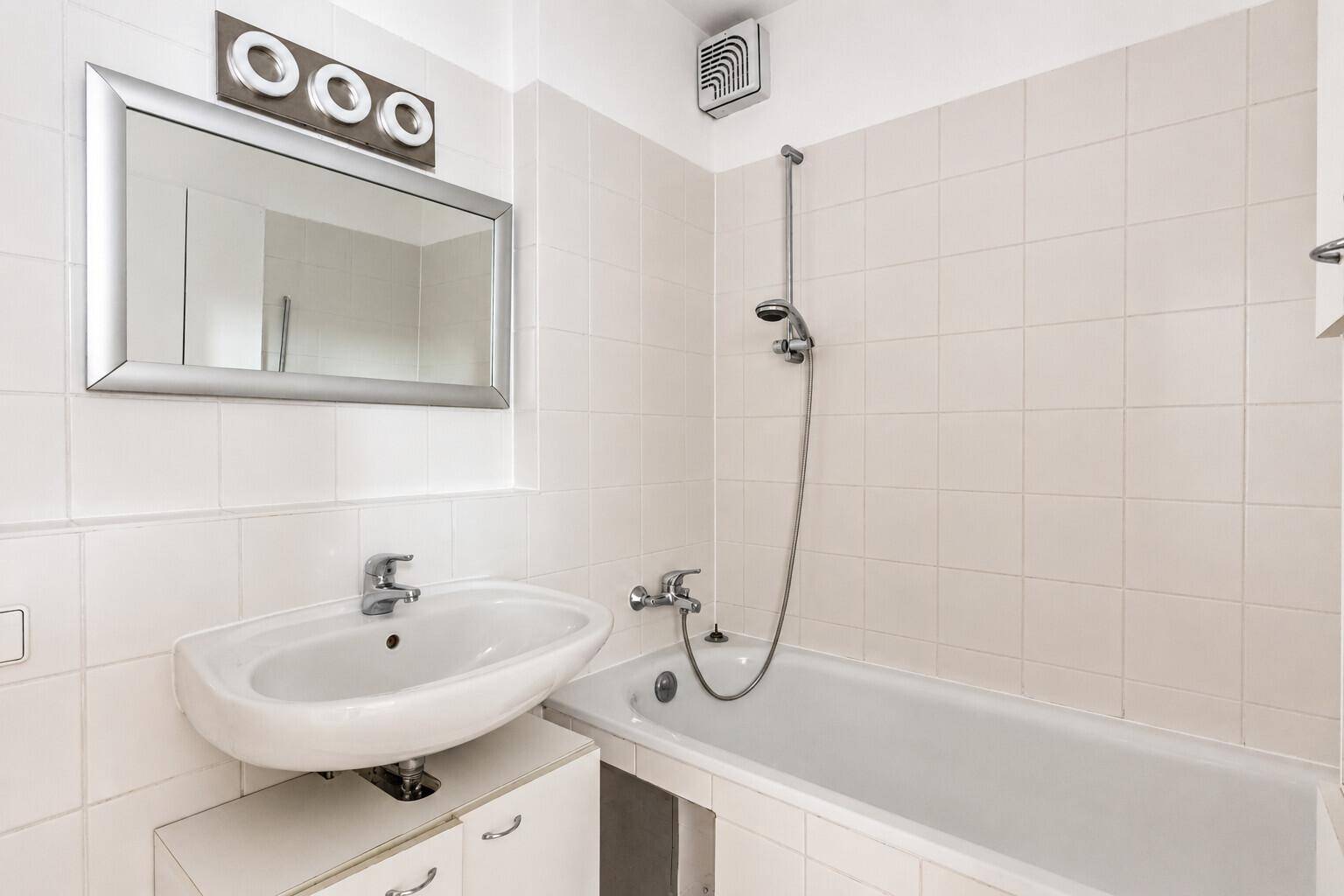 Gefliestes Badezimmer mit Badewanne, Duschfunktion, Waschbecken und einem Spiegel über dem Waschtisch.