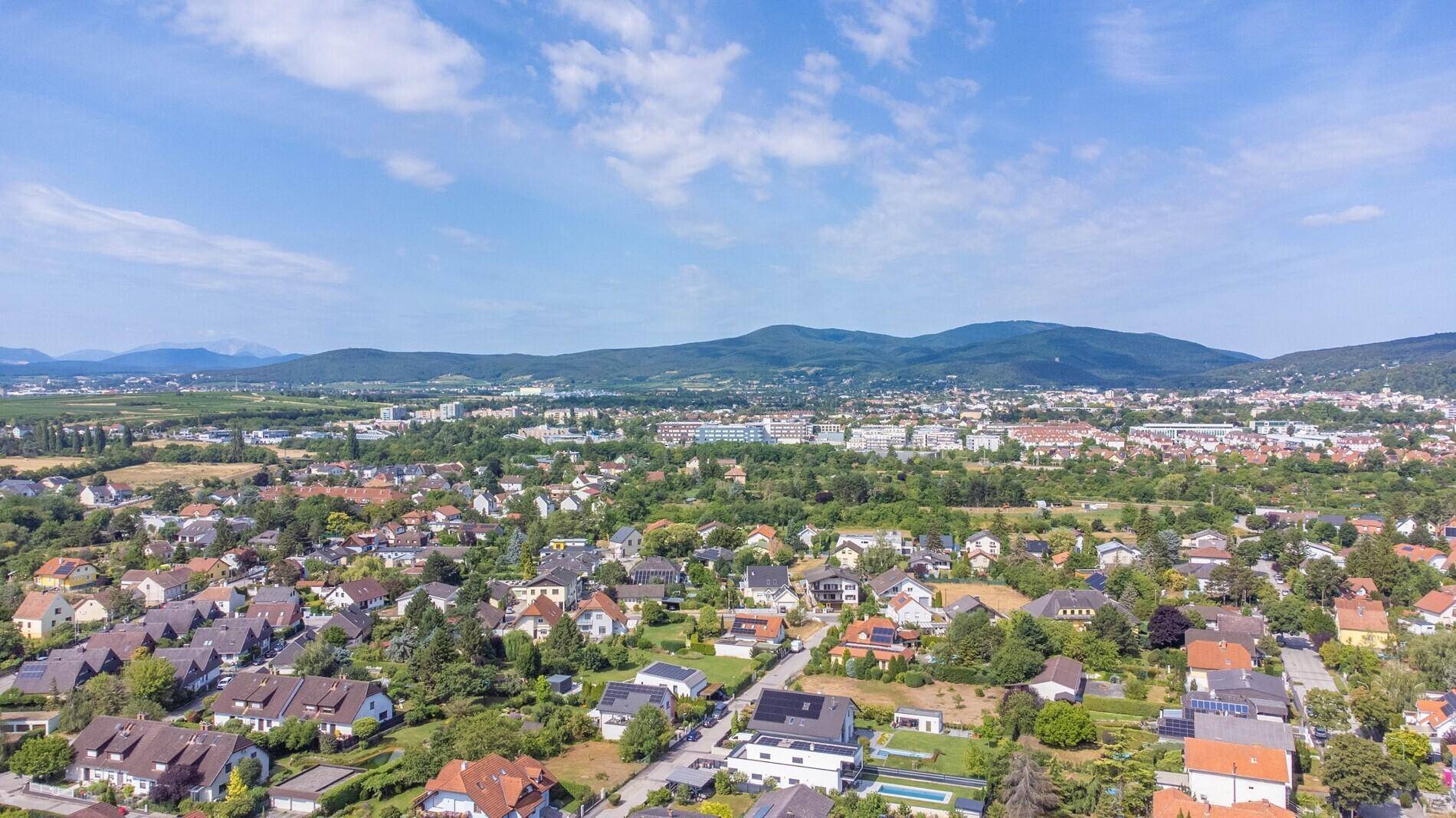 Weitläufige Luftaufnahme einer Siedlung mit Häusern und grüner Landschaft im Hintergrund.