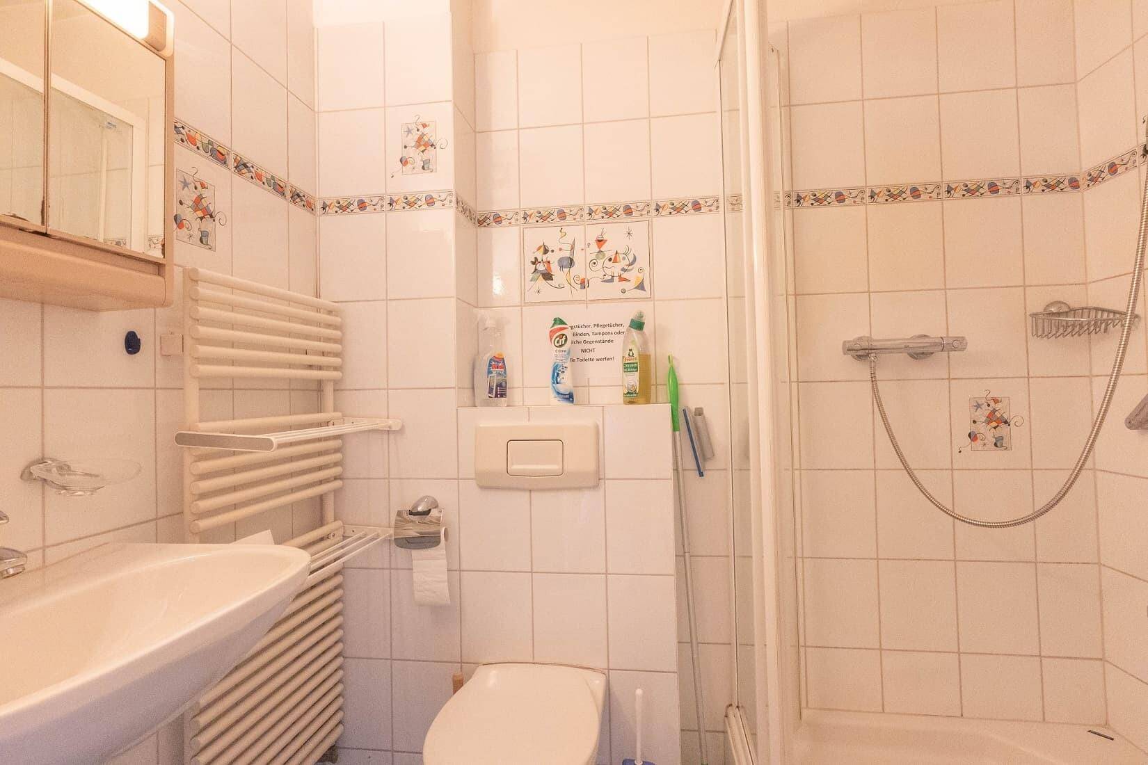 Gefliestes Badezimmer mit Dusche, WC, Waschbecken und beheiztem Handtuchhalter.