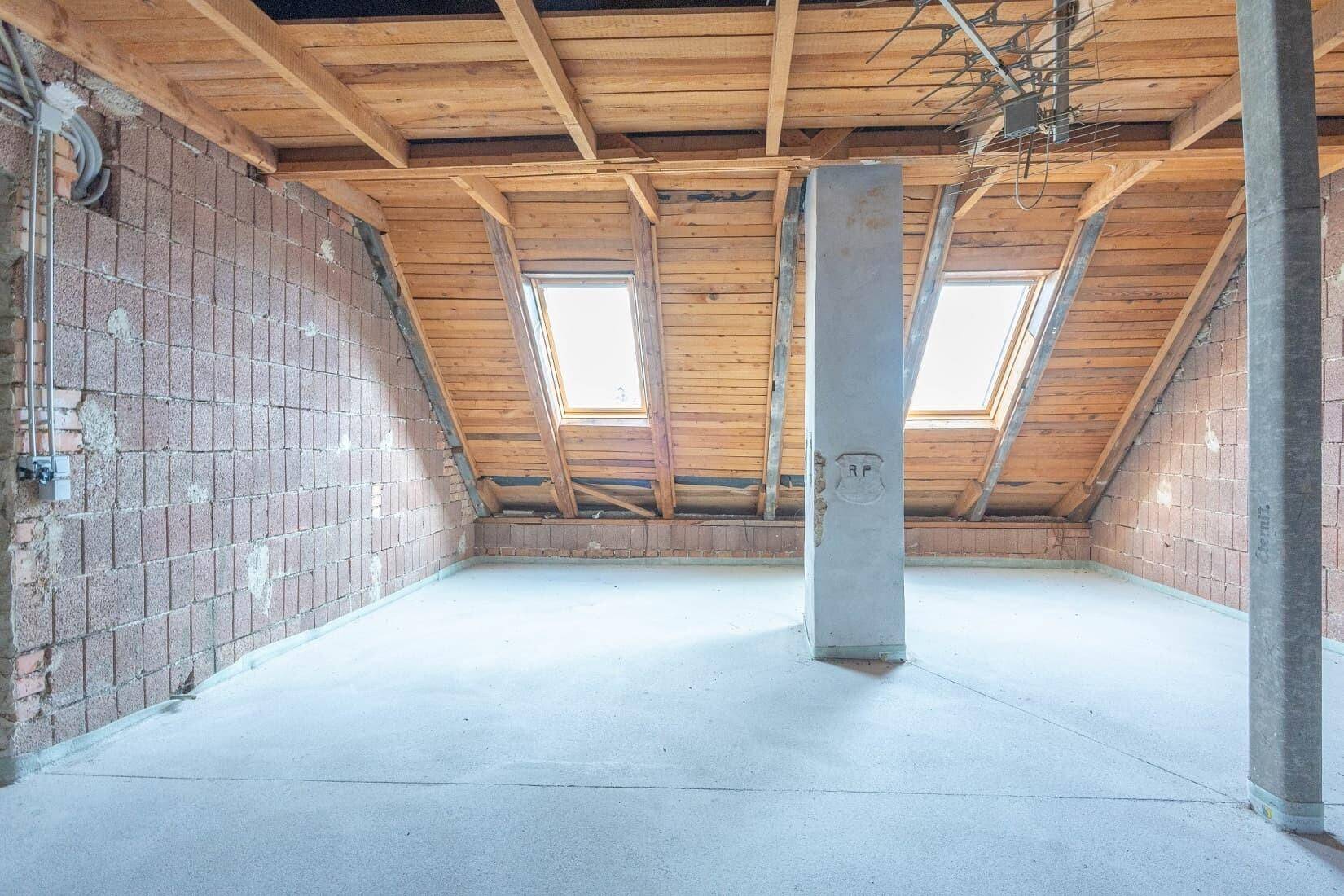 Dachboden mit Holzbalken, Ziegelwänden und Dachfenstern, ideal für zukünftige Nutzung.