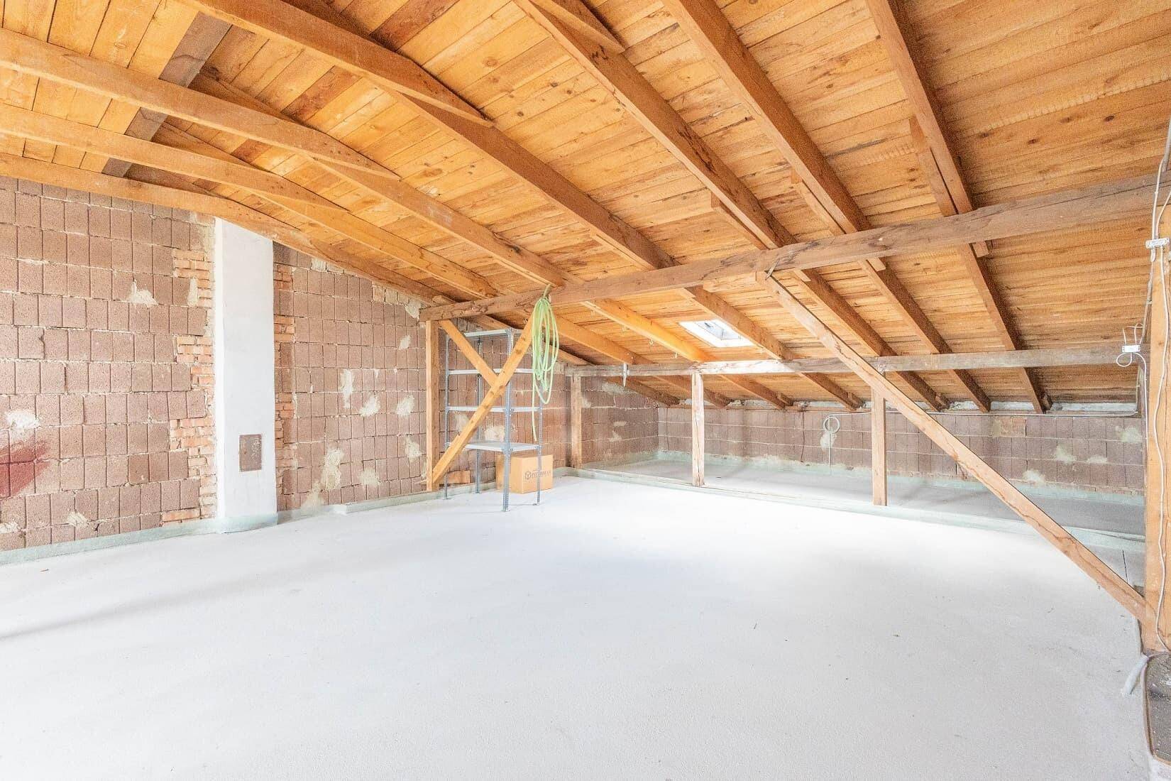 Geräumiger Dachboden mit sichtbaren Holzbalken und Ziegelwänden, bereit für den Ausbau.