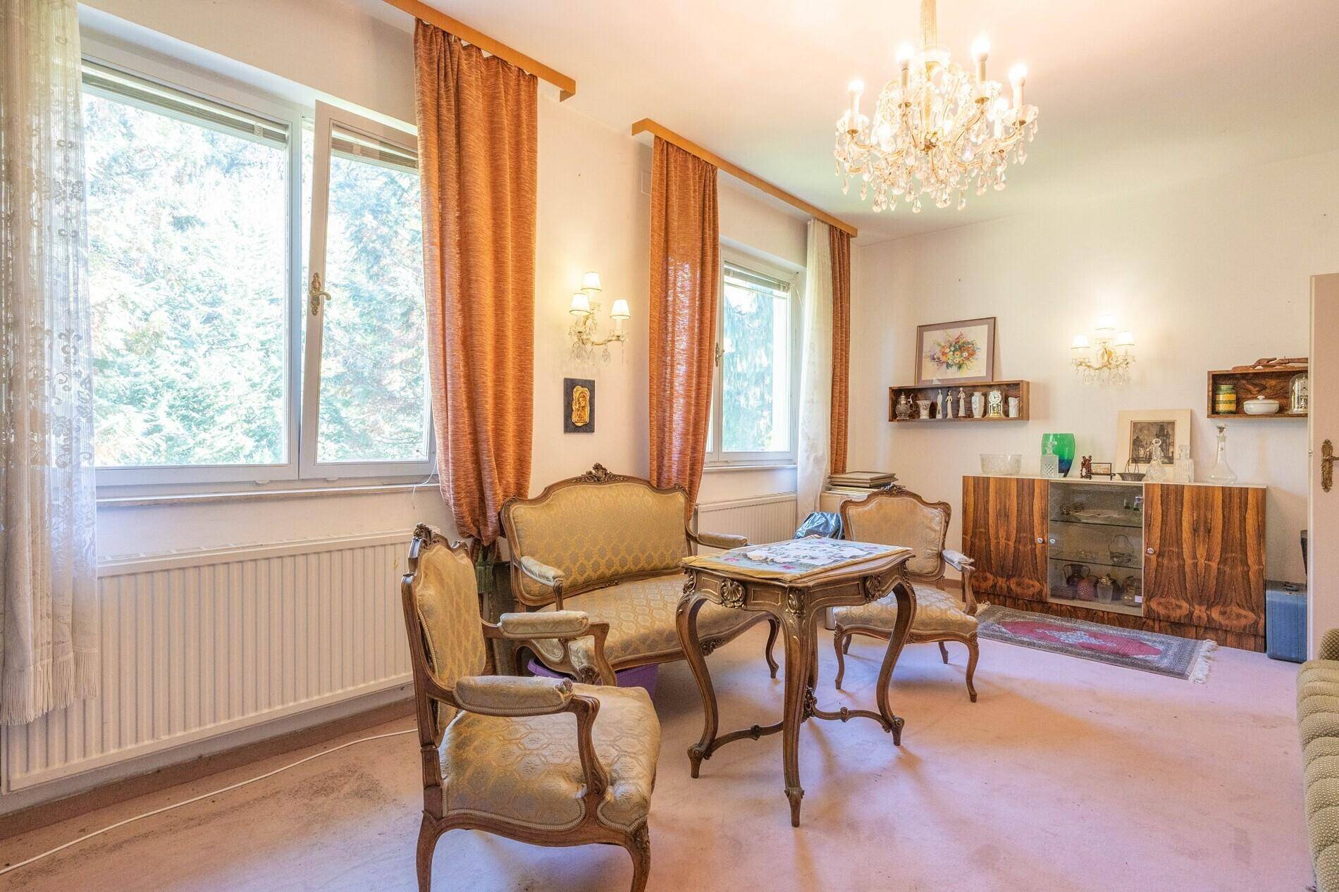 Helles Zimmer mit Teppichboden, großen Fenstern und klassischem Mobiliar.