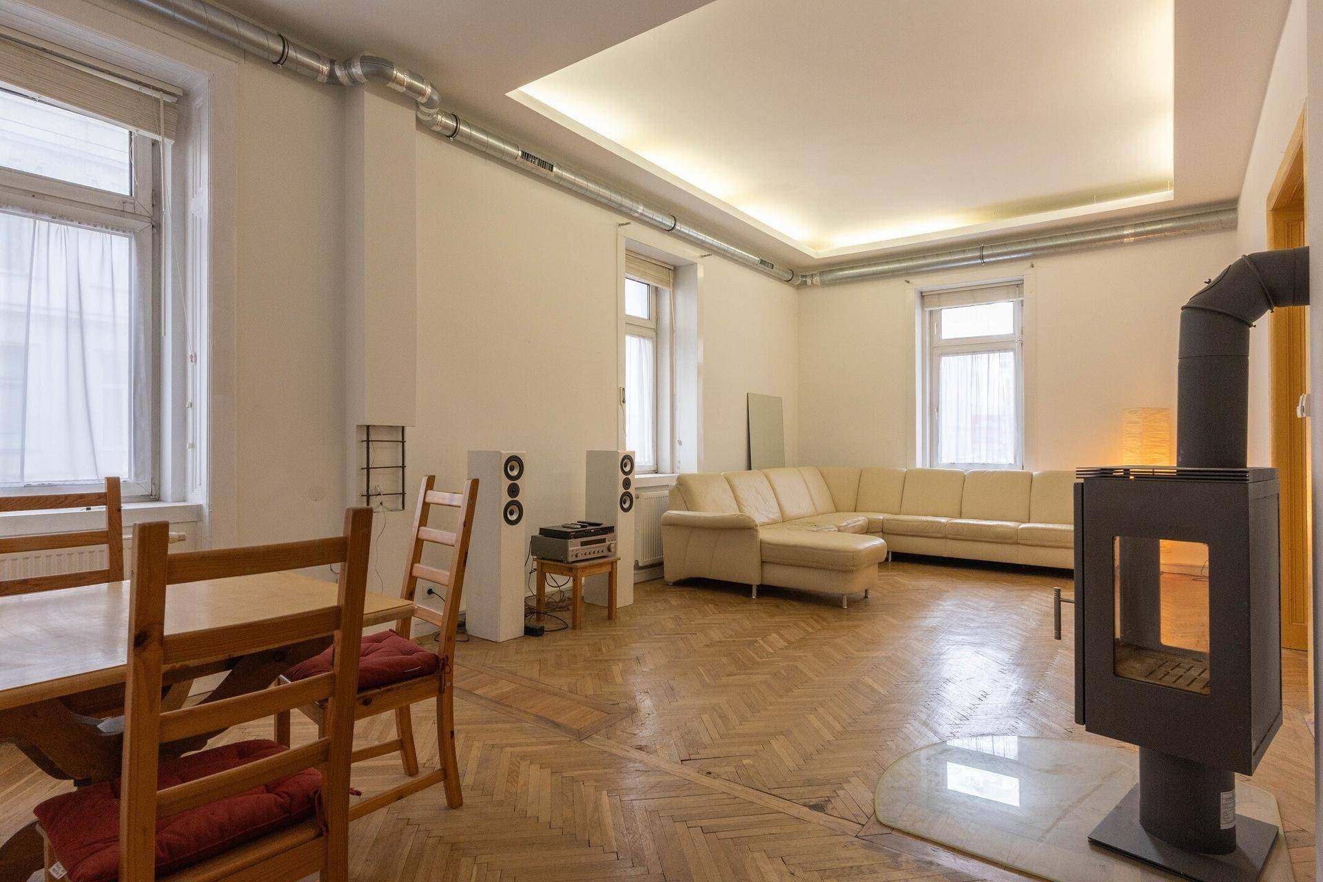 Geräumiges Wohn- und Esszimmer mit Fischgrätparkett, Kaminofen und großer Eckcouch.