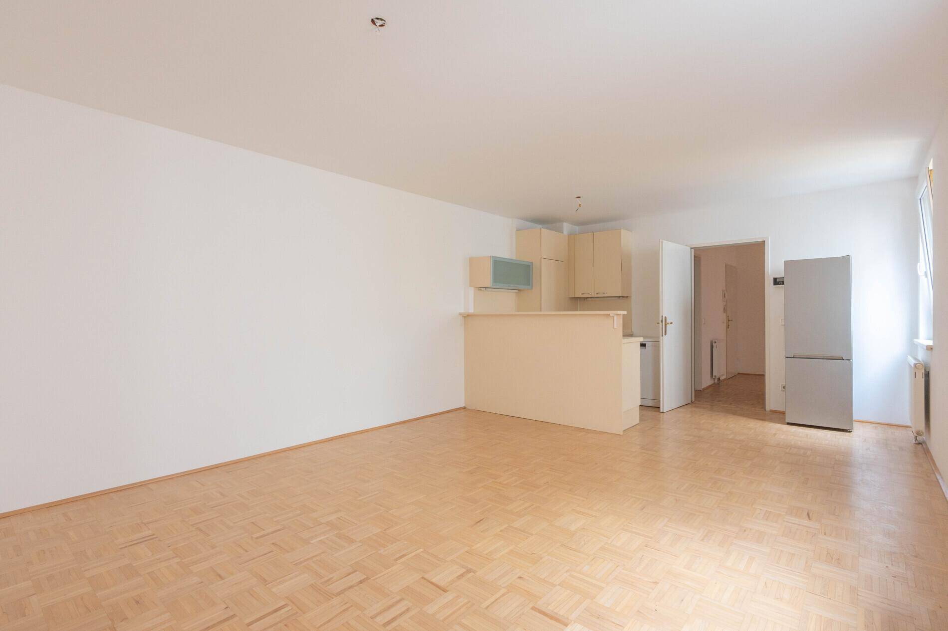 Geräumiger Wohnbereich mit heller Parkettboden und integrierter Küchenzeile, ideal für offenes Wohnen.