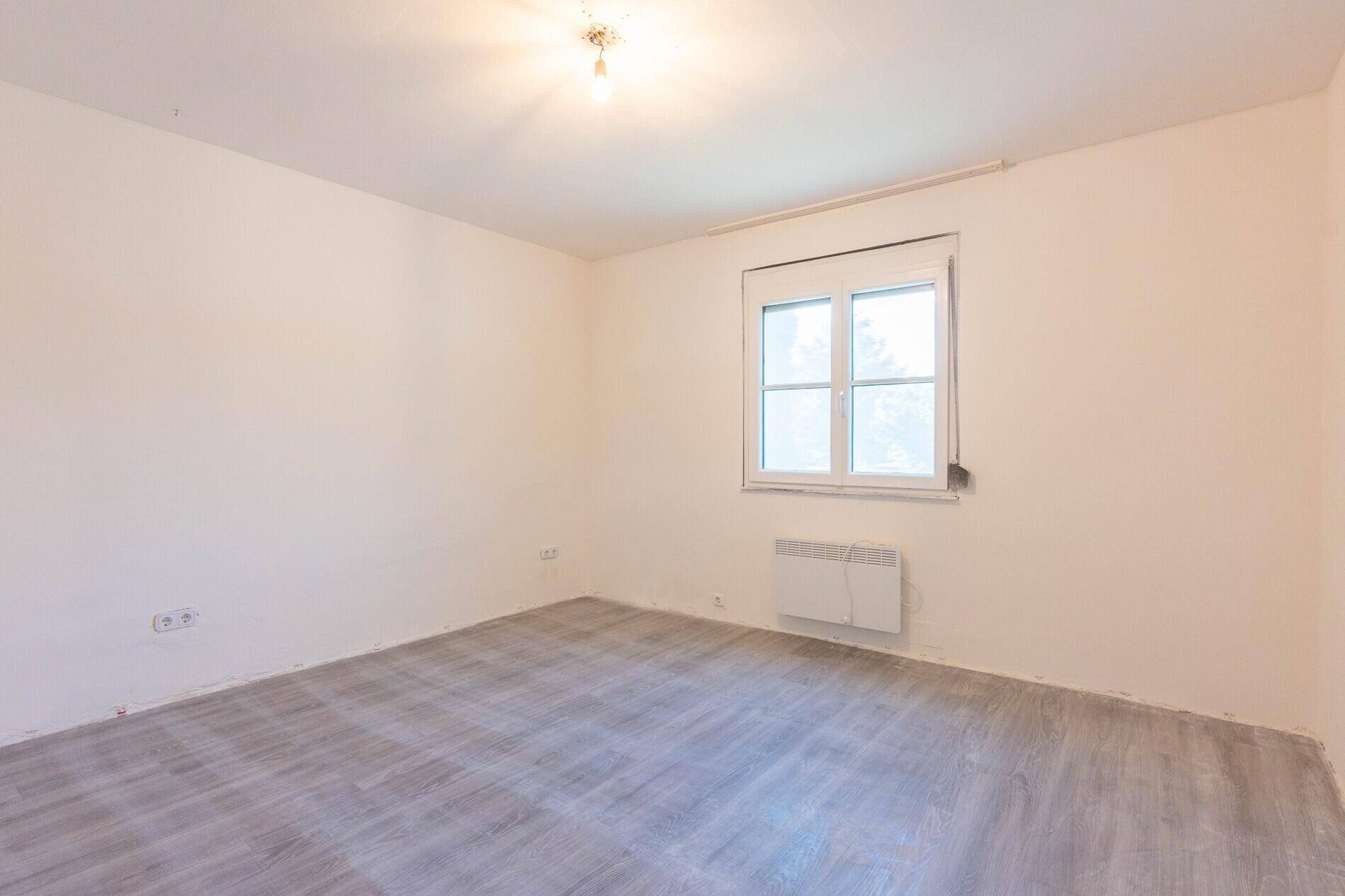 Helles Schlafzimmer mit Laminatboden und großem Fenster, bereit zur individuellen Gestaltung.