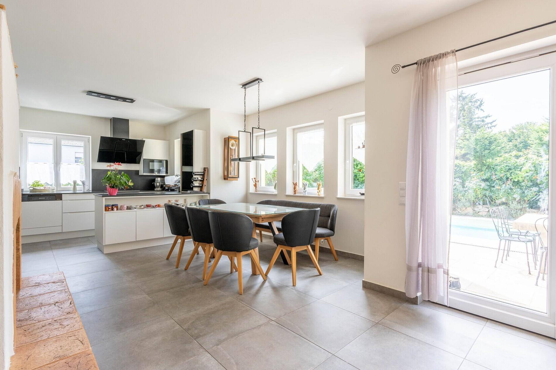Heller offener Wohn-Essbereich mit moderner Küche, Fliesenboden und Zugang zur Terrasse.