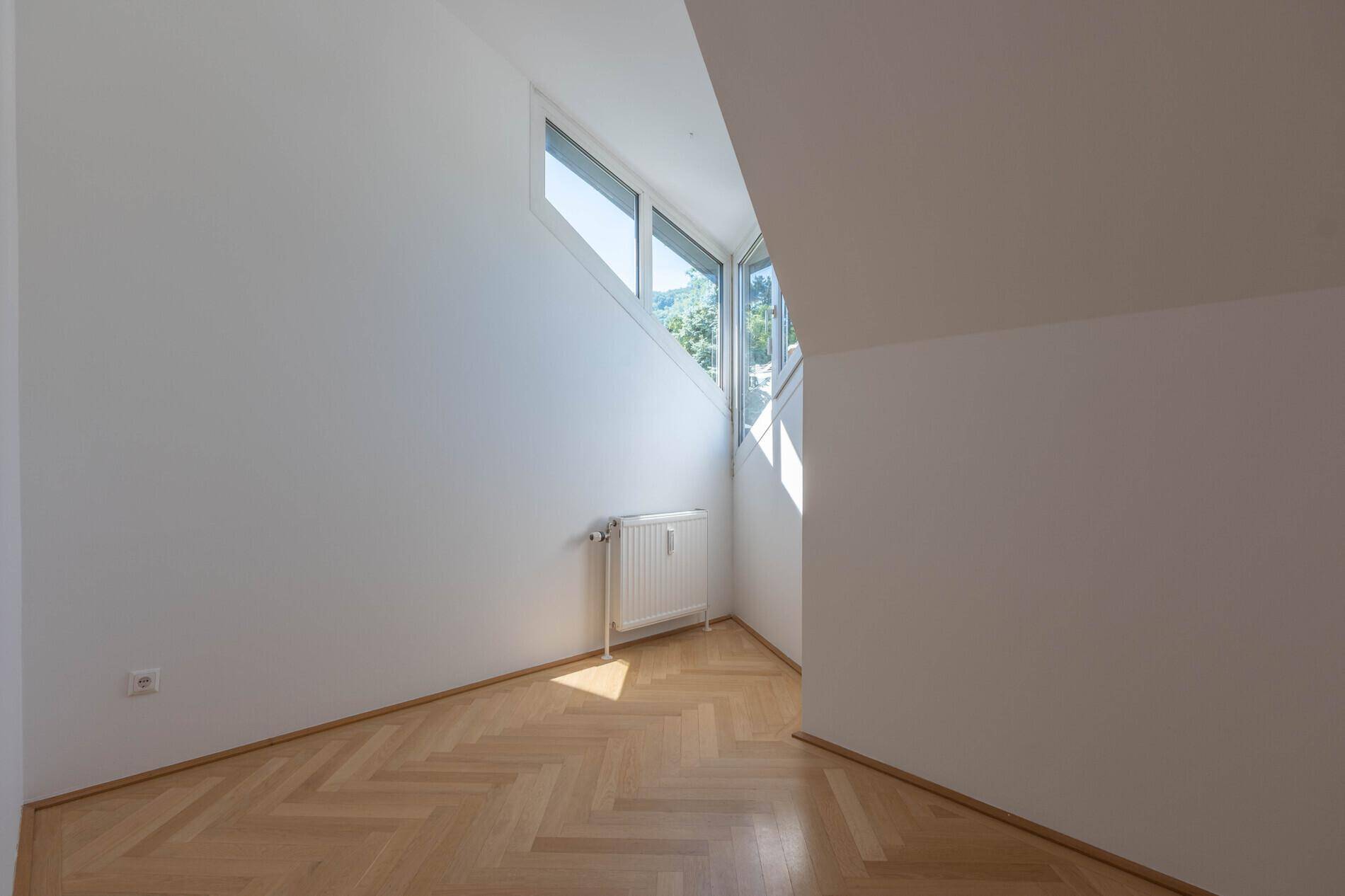 Helles Zimmer im Dachgeschoss mit schrägen Wänden, Fischgrätparkett und Dachfenstern.
