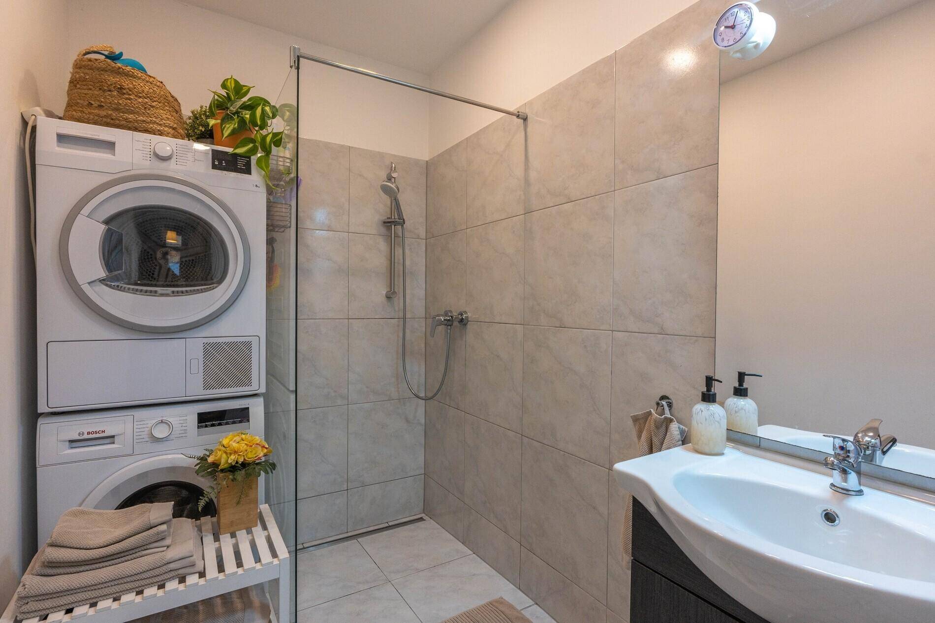Modernes Badezimmer mit ebenerdiger Dusche, Waschbecken und integrierter Waschmaschine und Trockner.