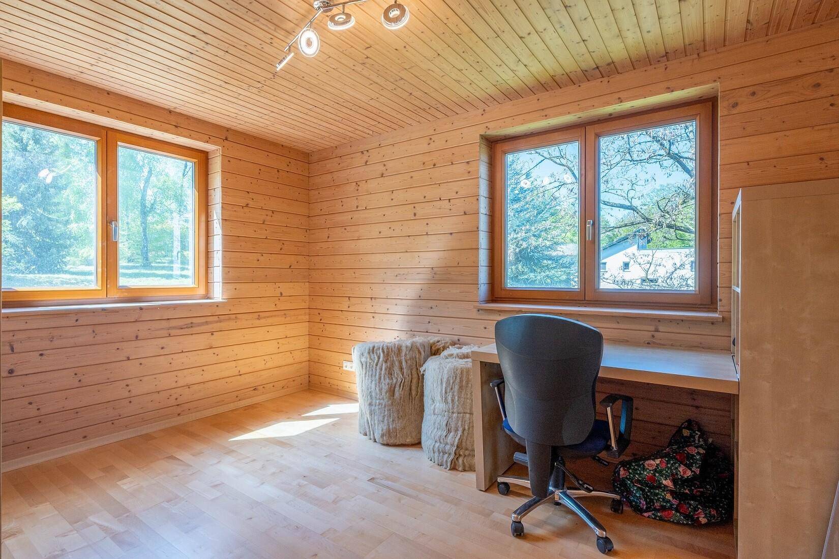 Schlafzimmer mit Holzwänden, Holzboden und zwei großen Fenstern mit Blick ins Grüne.