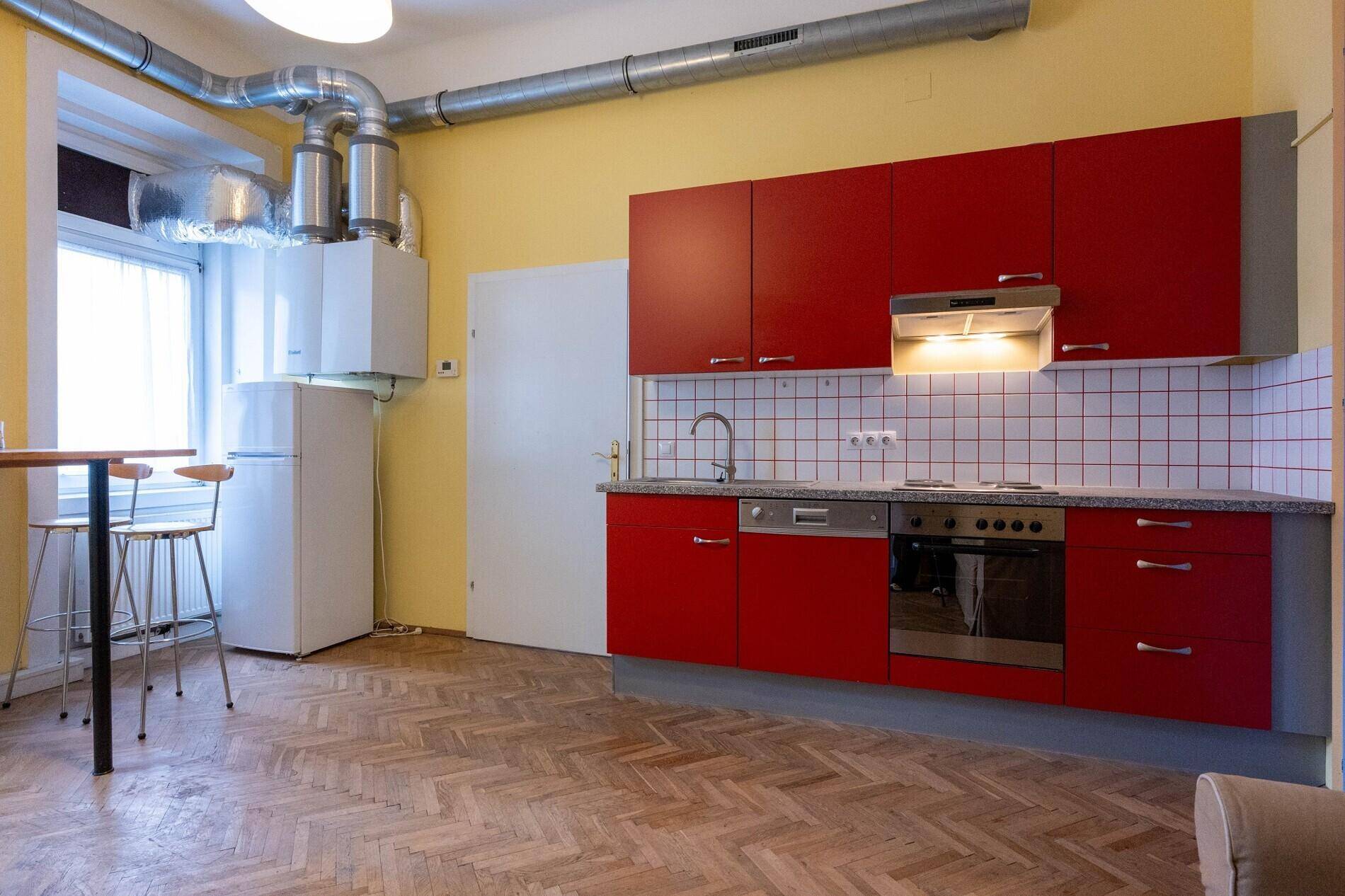 Küche mit roten Schränken, Fliesenrückwand und freistehendem Kühlschrank.