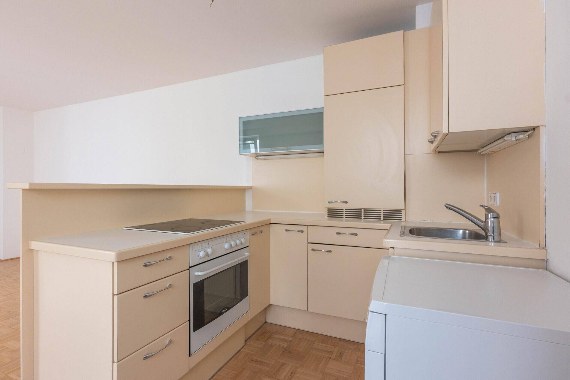 Funktionale Küchenzeile mit beigen Schränken, Kochfeld, Backofen und Spüle, bereit zur Nutzung.