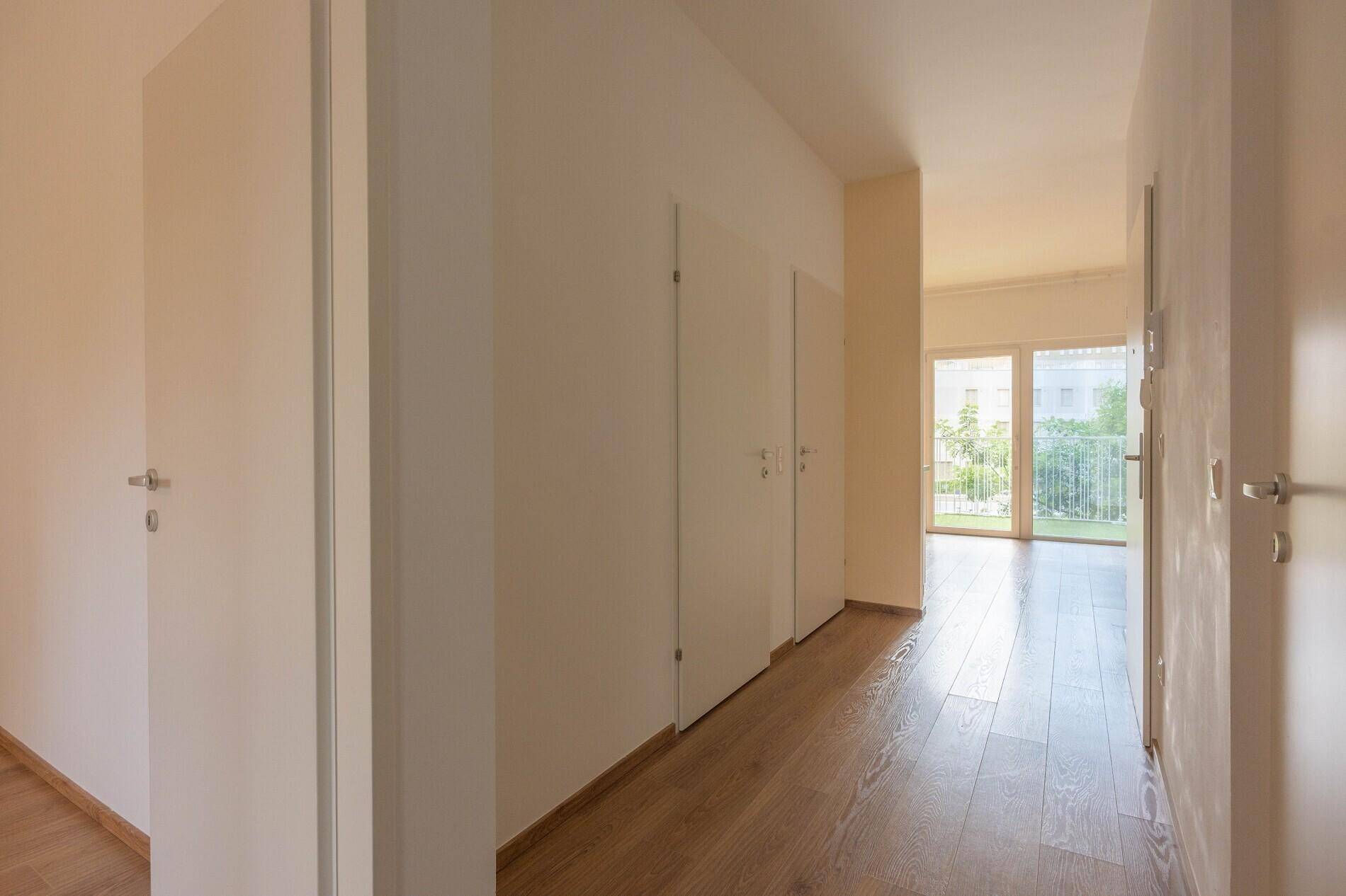 Heller Flur mit Holzboden und weißen Türen, der zu weiteren Räumen mit großen Fenstern führt.