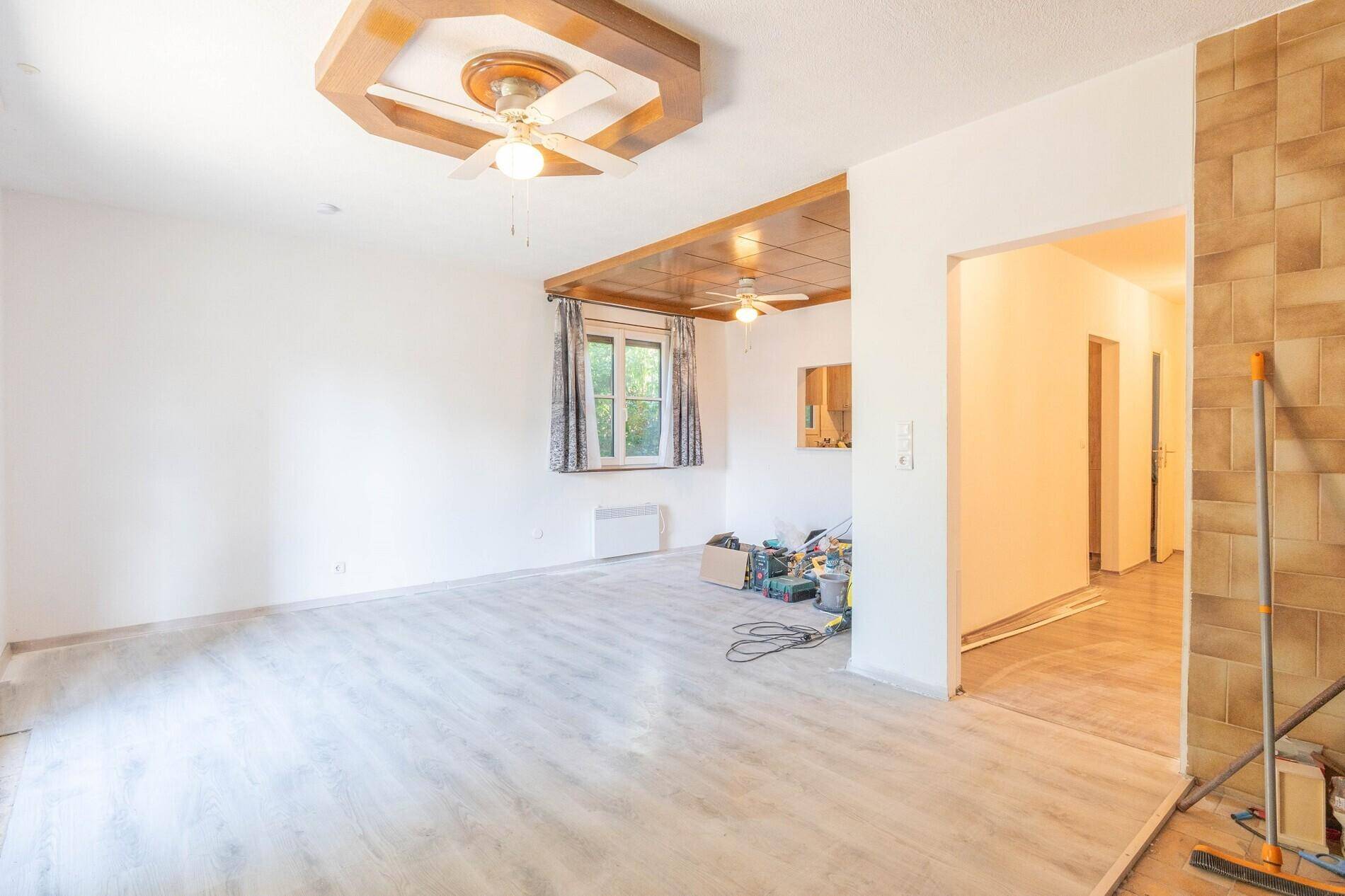 Helles Wohnzimmer mit hellem Laminatboden und Deckenventilatoren, bereit zur Renovierung.
