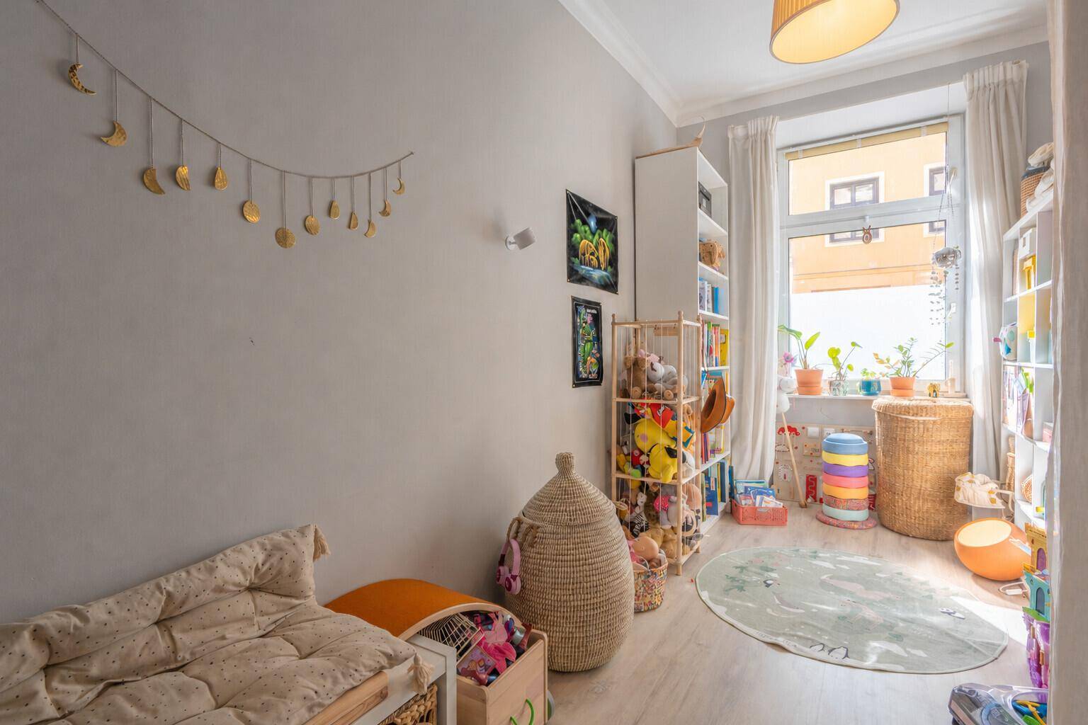 Helles Kinderzimmer mit Spielzeugregalen, Bodenmatratze und großem Fenster.