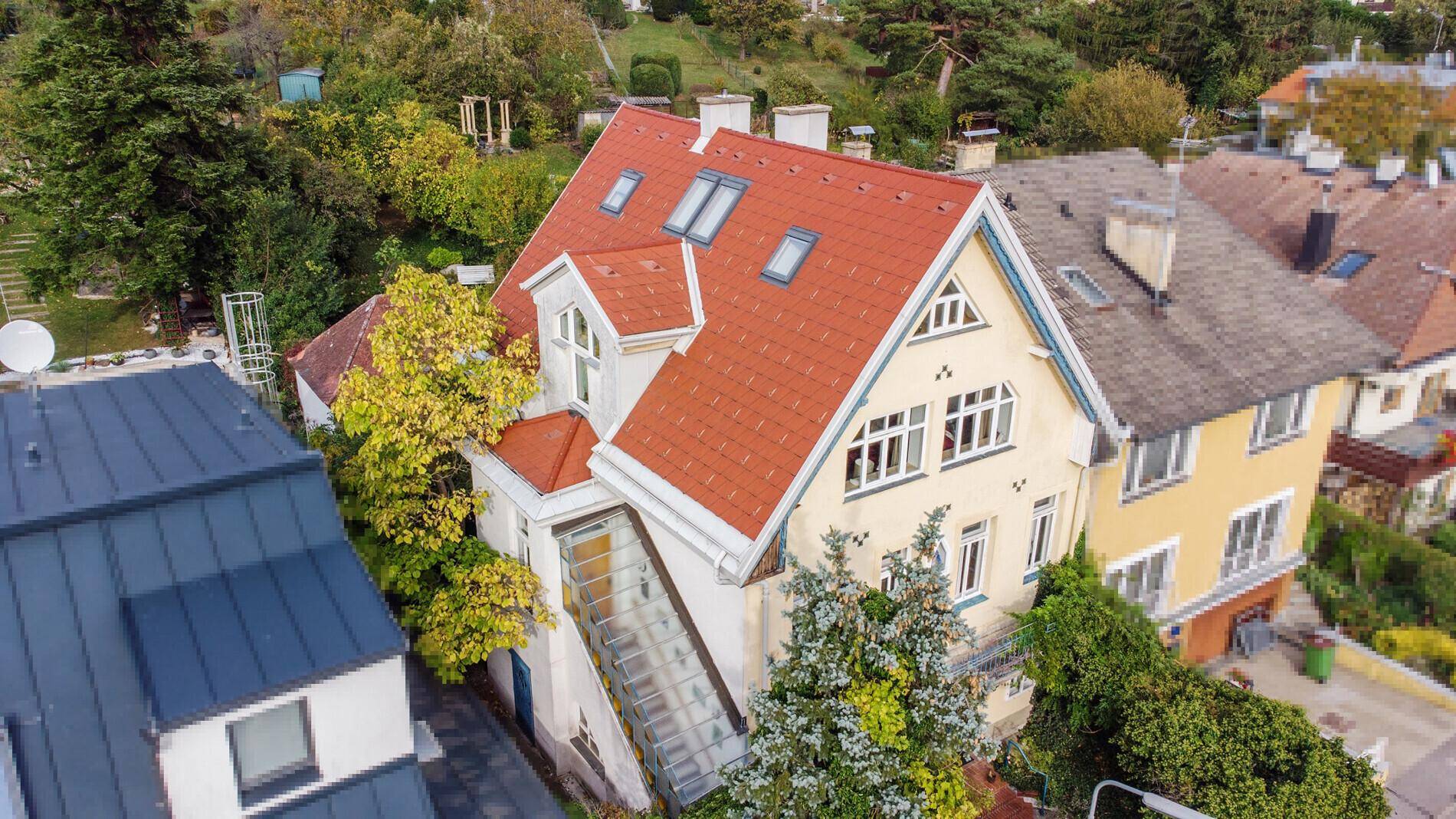 Historisches Gebäude mit rotem Ziegeldach und Gaubenfenstern, umgeben von viel Grün.