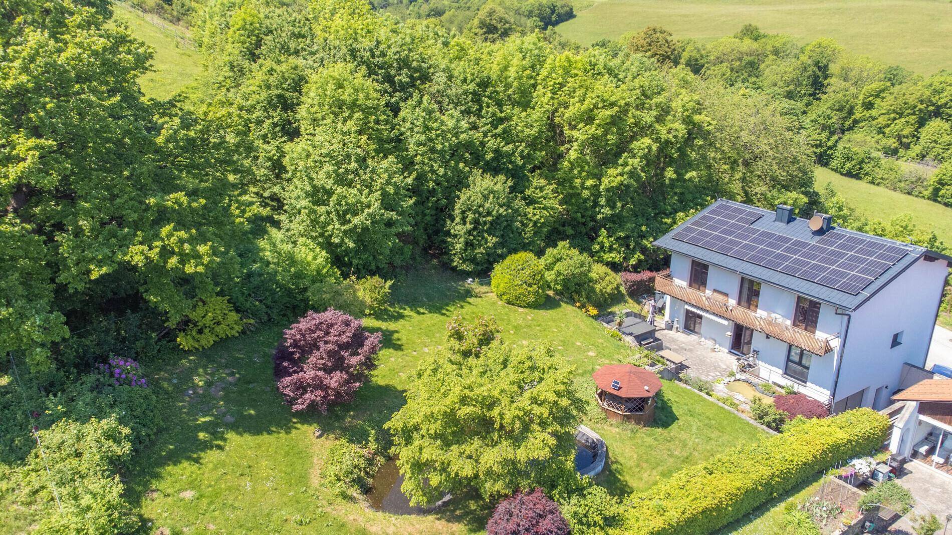 Haus mit Solaranlage, großer Terrasse und weitläufigem Garten mit Teich.