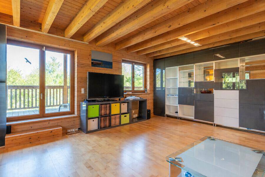Gemütliches Wohnzimmer mit Holzwänden, Holzbalkendecke und großem Fernseher.