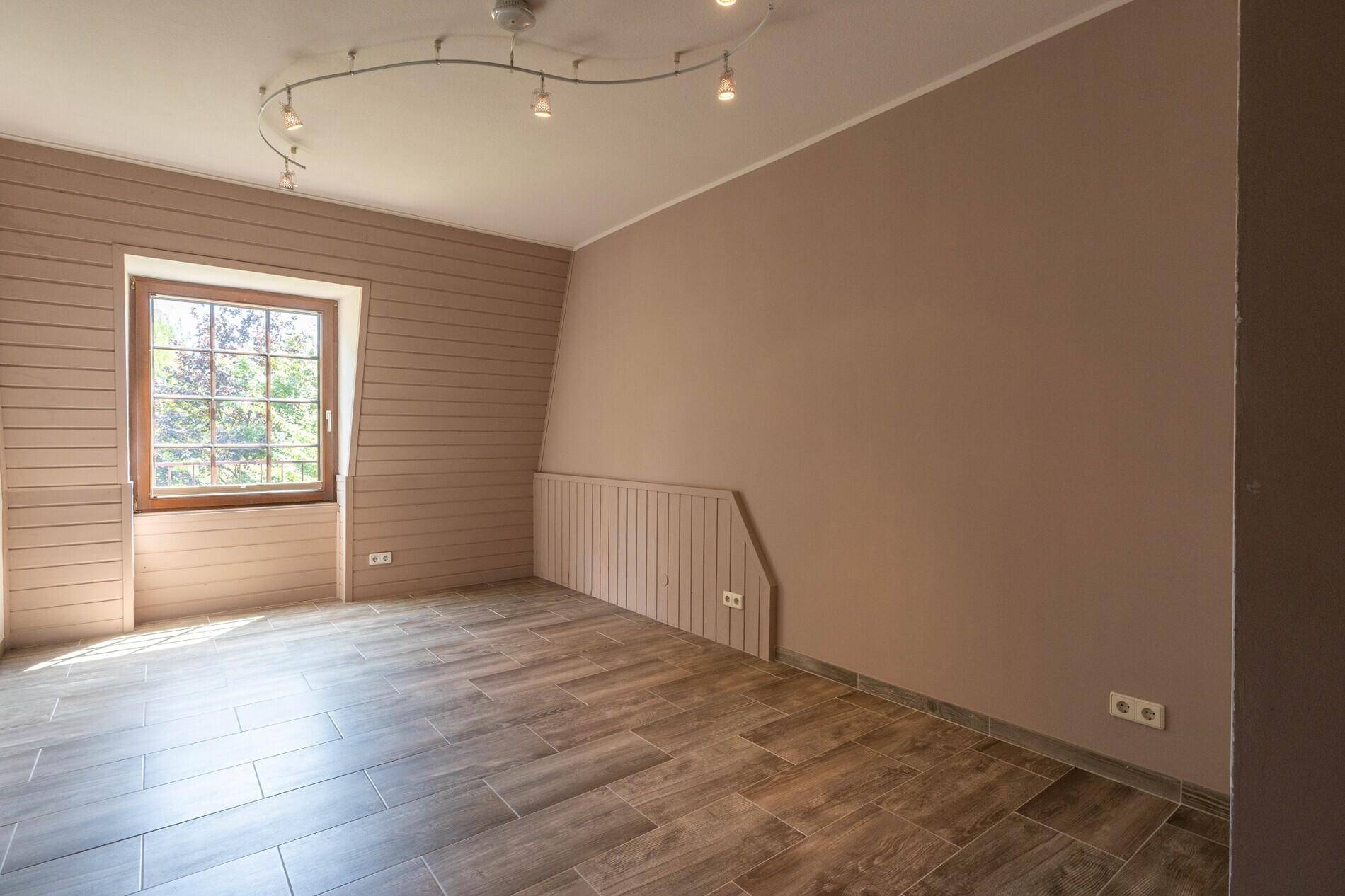 Gemütliches Zimmer mit taupefarbenen Wänden, Holzvertäfelung und Fliesenboden in Holzoptik.