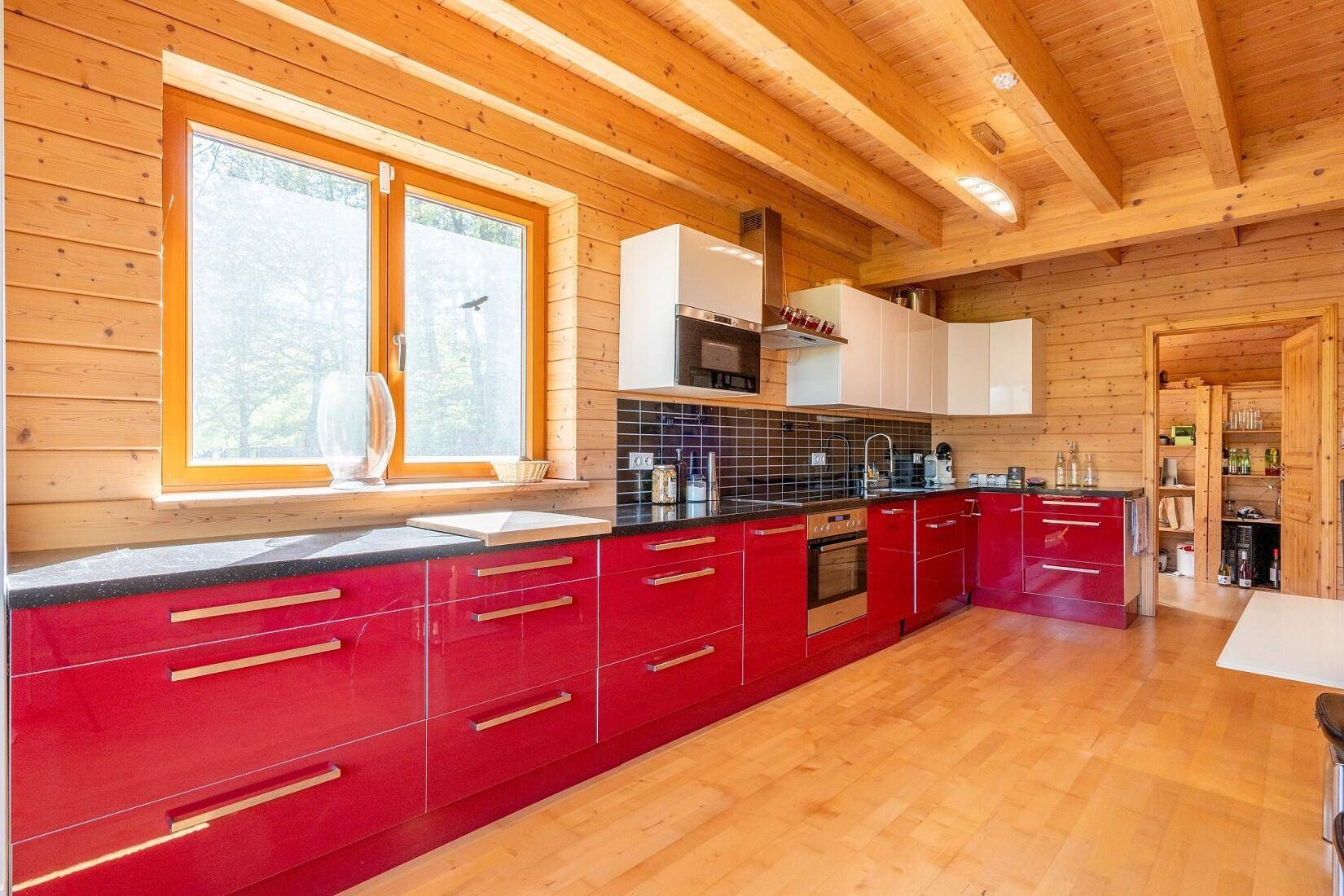 Moderne Küche mit roten Hochglanzfronten, schwarzen Arbeitsplatten und Holzwänden.