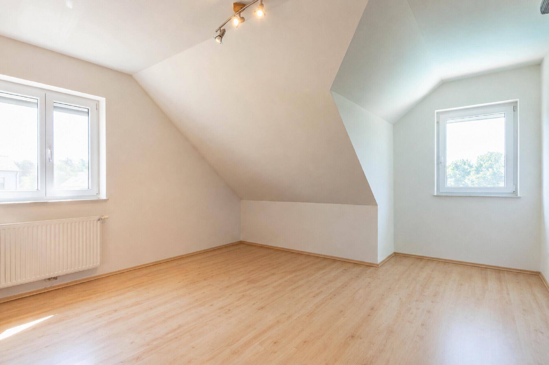 Leeres Zimmer im Dachgeschoss mit schrägen Wänden, Laminatboden und Fenstern.