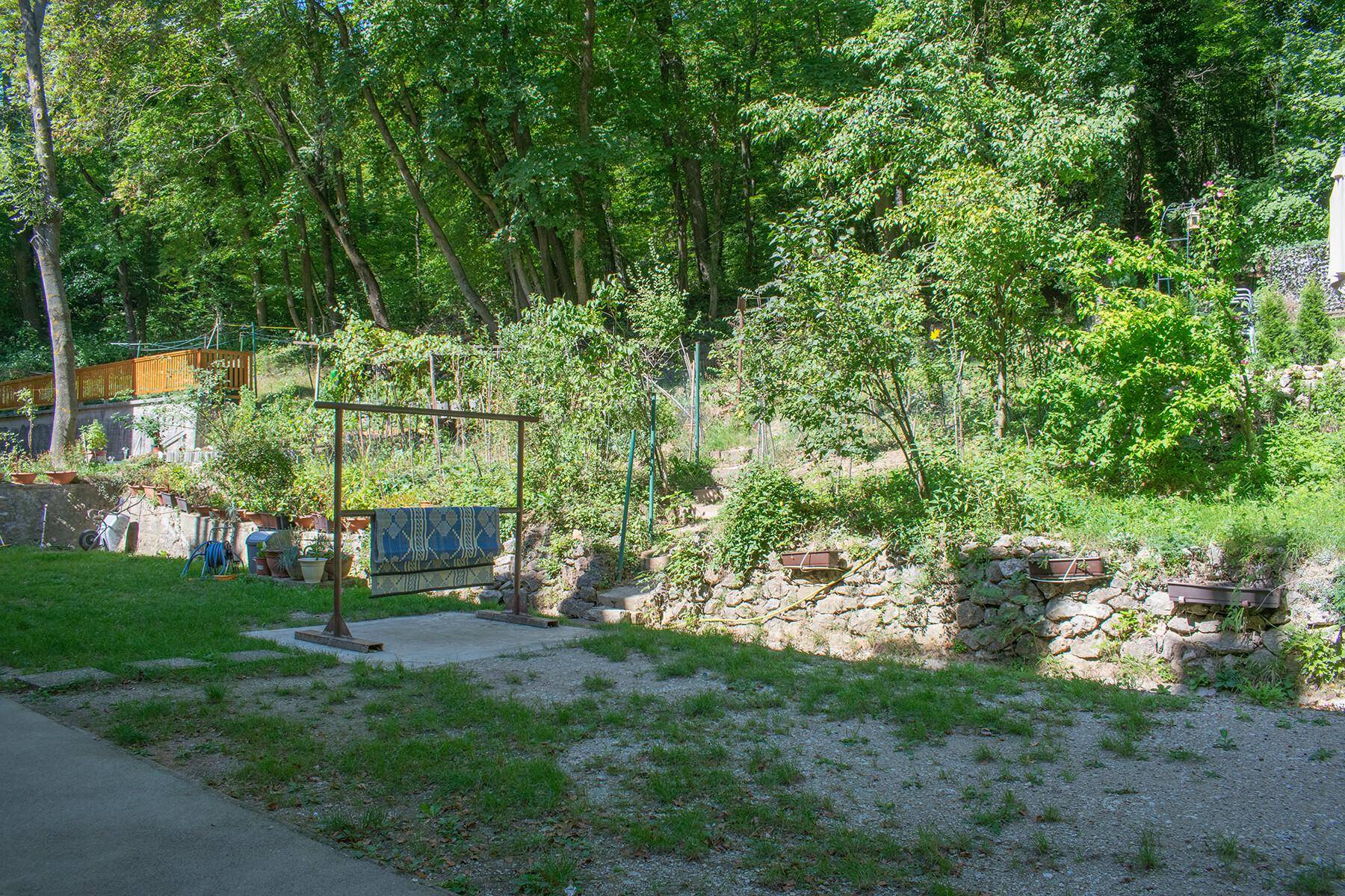 Terrassierter Gartenbereich mit Steinmauern, Pflanzen und Blick auf bewaldete Hänge.