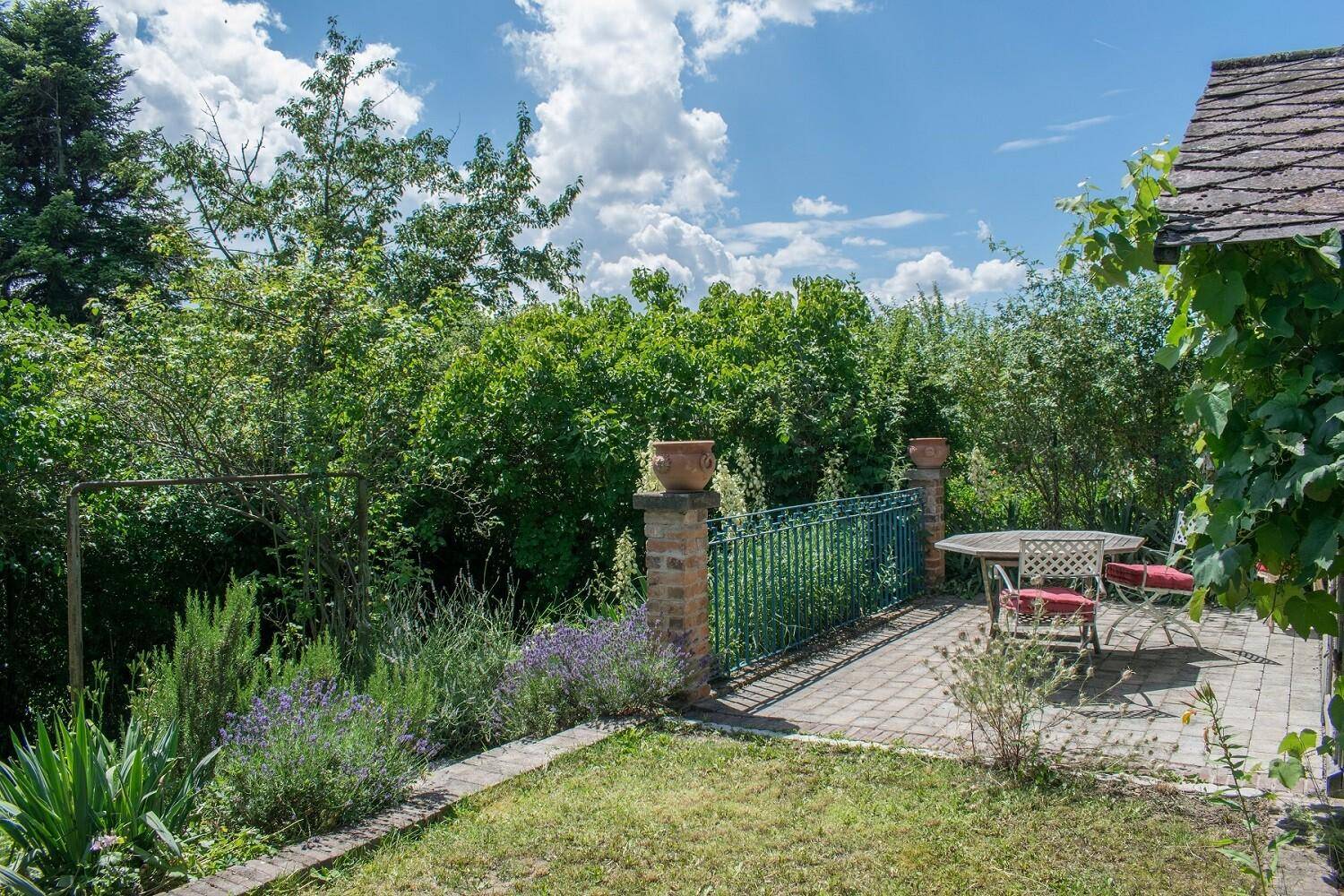 Sonniger Terrassenbereich mit Pflastersteinen, Gartenmöbeln und Blick ins Grüne.