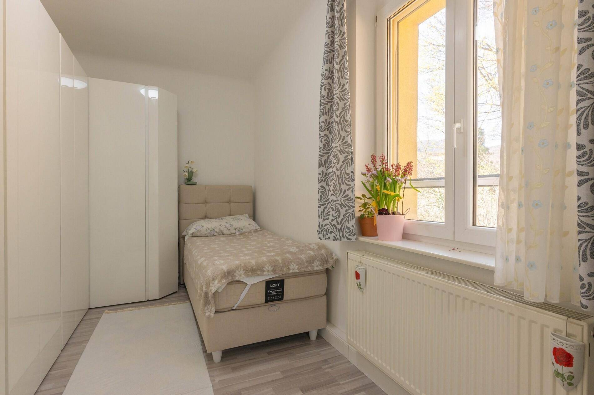 Gemütliches Schlafzimmer mit Einzelbett, weißem Kleiderschrank und Fenster mit Tageslicht.