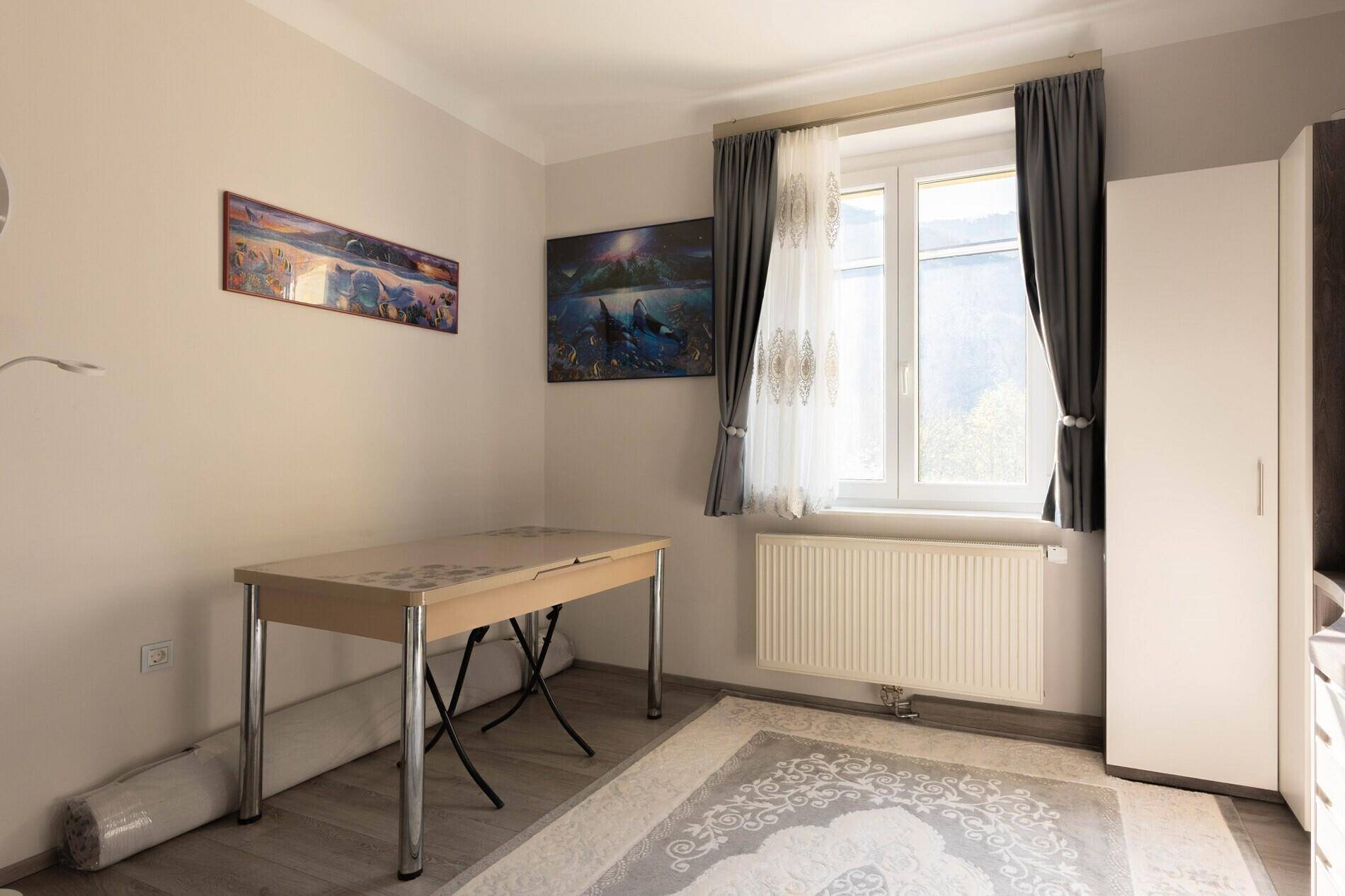 Heller Raum mit kleinem Tisch, Kleiderschrank und Fenster mit Blick ins Grüne.
